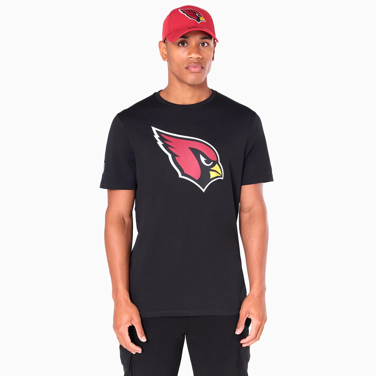 New Era Arizona Cardinals NFL Black T-Shirt, on-model view showing the large red cardinal logo centred on the chest of the black t-shirt, worn by a person also wearing a red cap with a raised cardinal logo on the front.