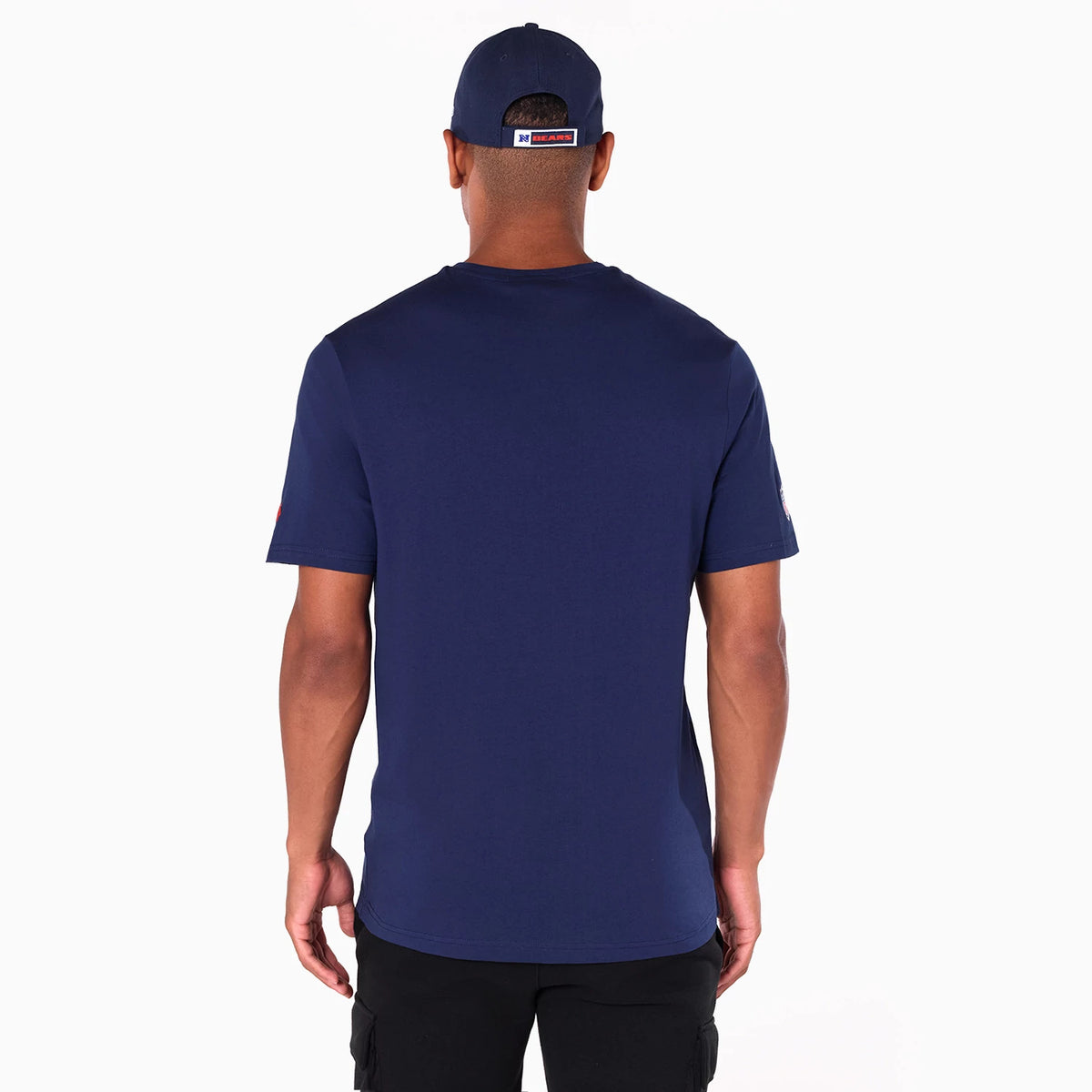 New Era Chicago Bears NFL Navy T-Shirt, rear view showing the solid navy back with short sleeves, worn by a person, paired with a navy cap featuring a raised Bears logo on the back above an orange panel.