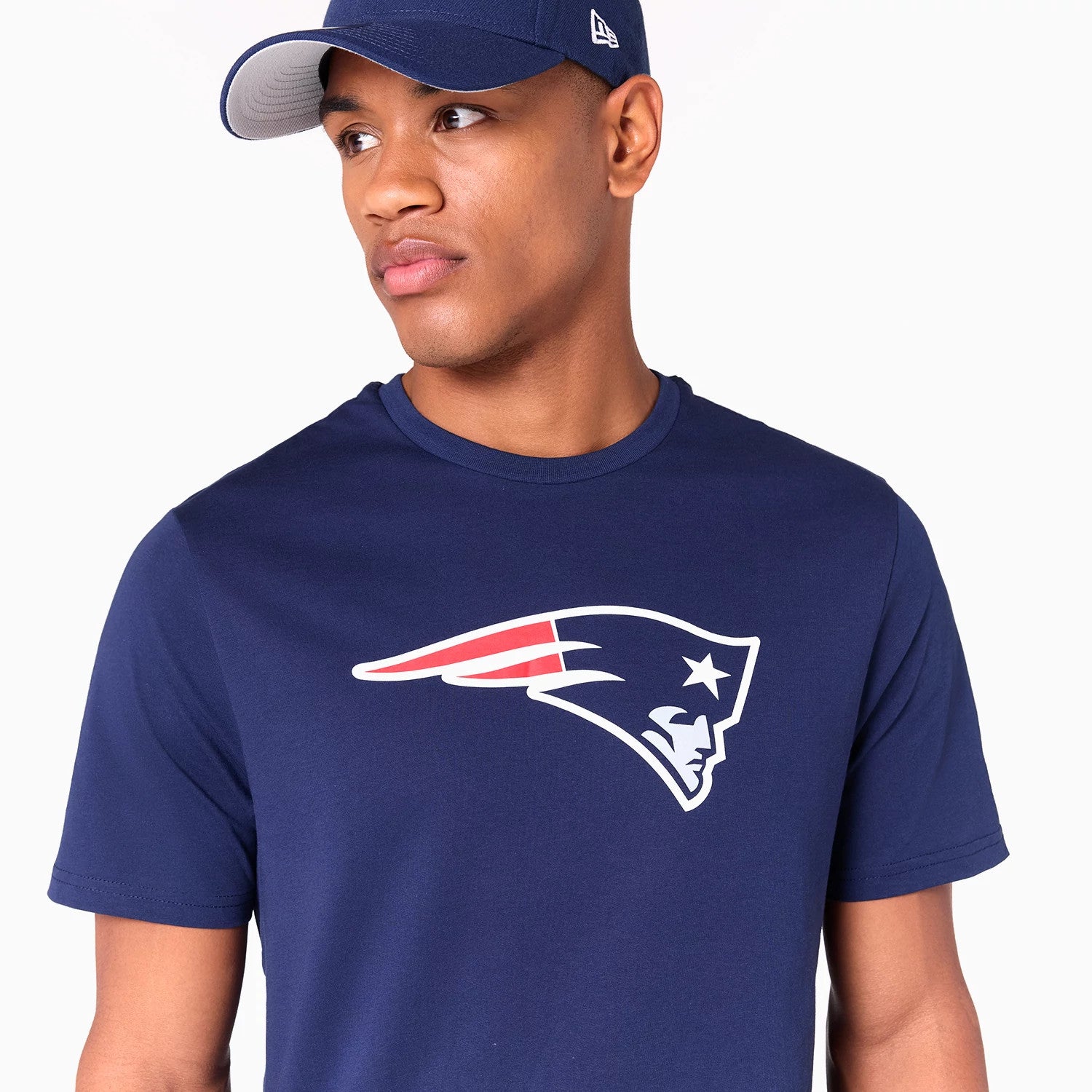 New Era New England Patriots NFL Navy T-Shirt, on-model view showing the short-sleeved navy shirt with the Patriots logo printed in white and red on the chest, paired with a navy cap featuring a raised New Era logo on the side.