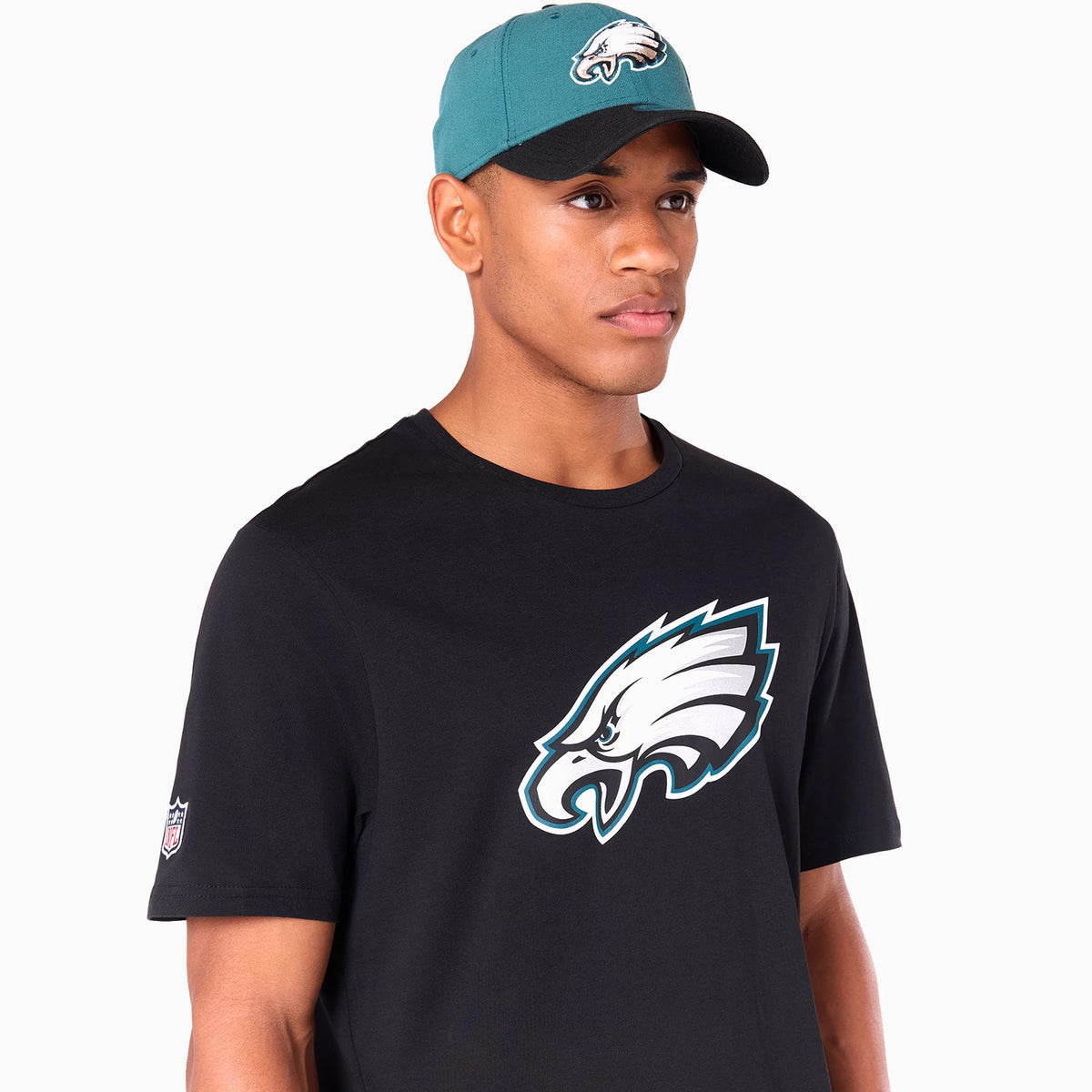 New Era Philadelphia Eagles NFL Black T-Shirt, on-model view showing the large white eagle logo printed across the chest and an additional small logo on the left sleeve, paired with a green cap featuring a raised eagle logo on the front panel.