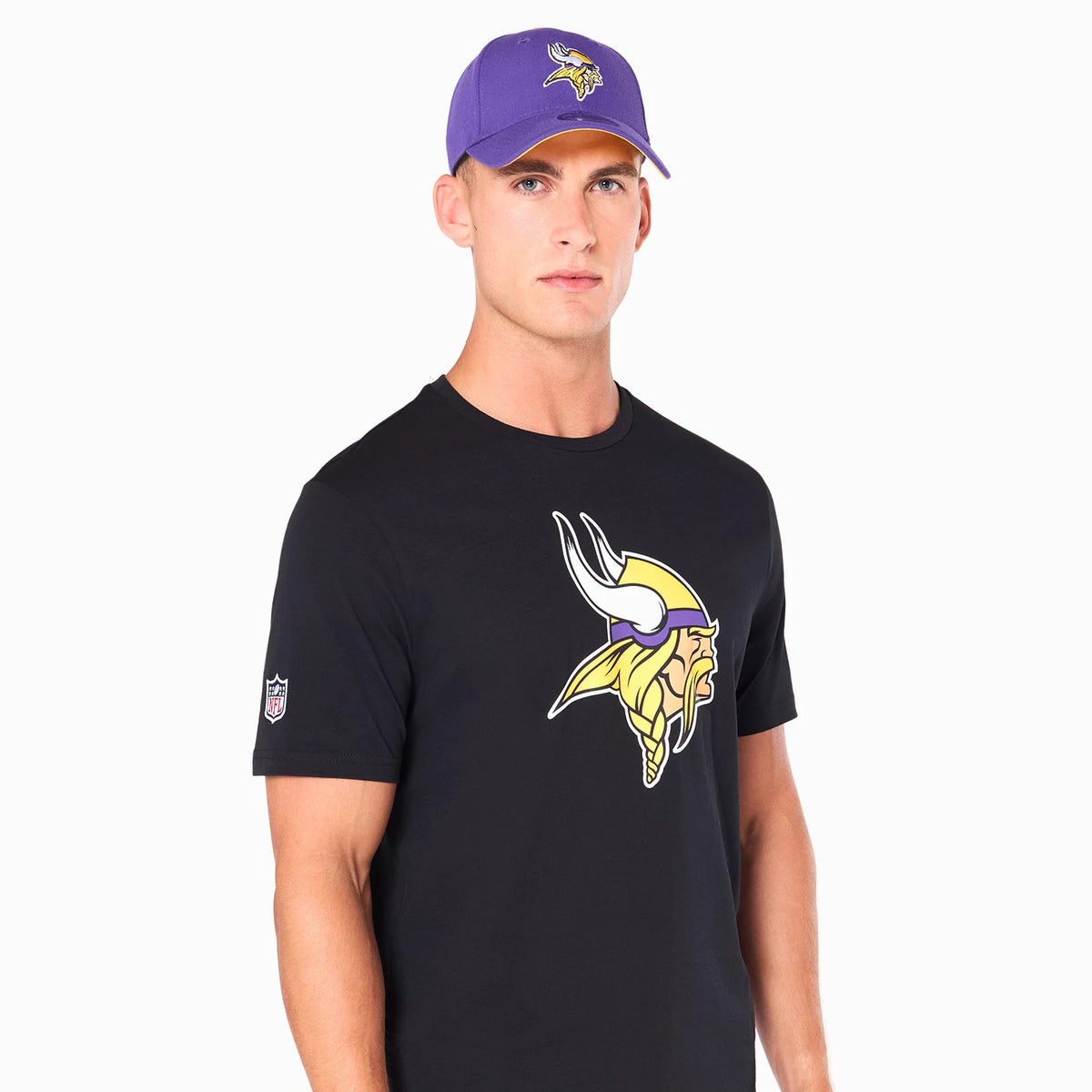 New Era Minnesota Vikings NFL Black T-Shirt, on-model view showing a black shirt with a large yellow and purple Vikings logo on the chest, a small NFL logo patch on the left sleeve, and a purple cap featuring the same logo worn by the model.