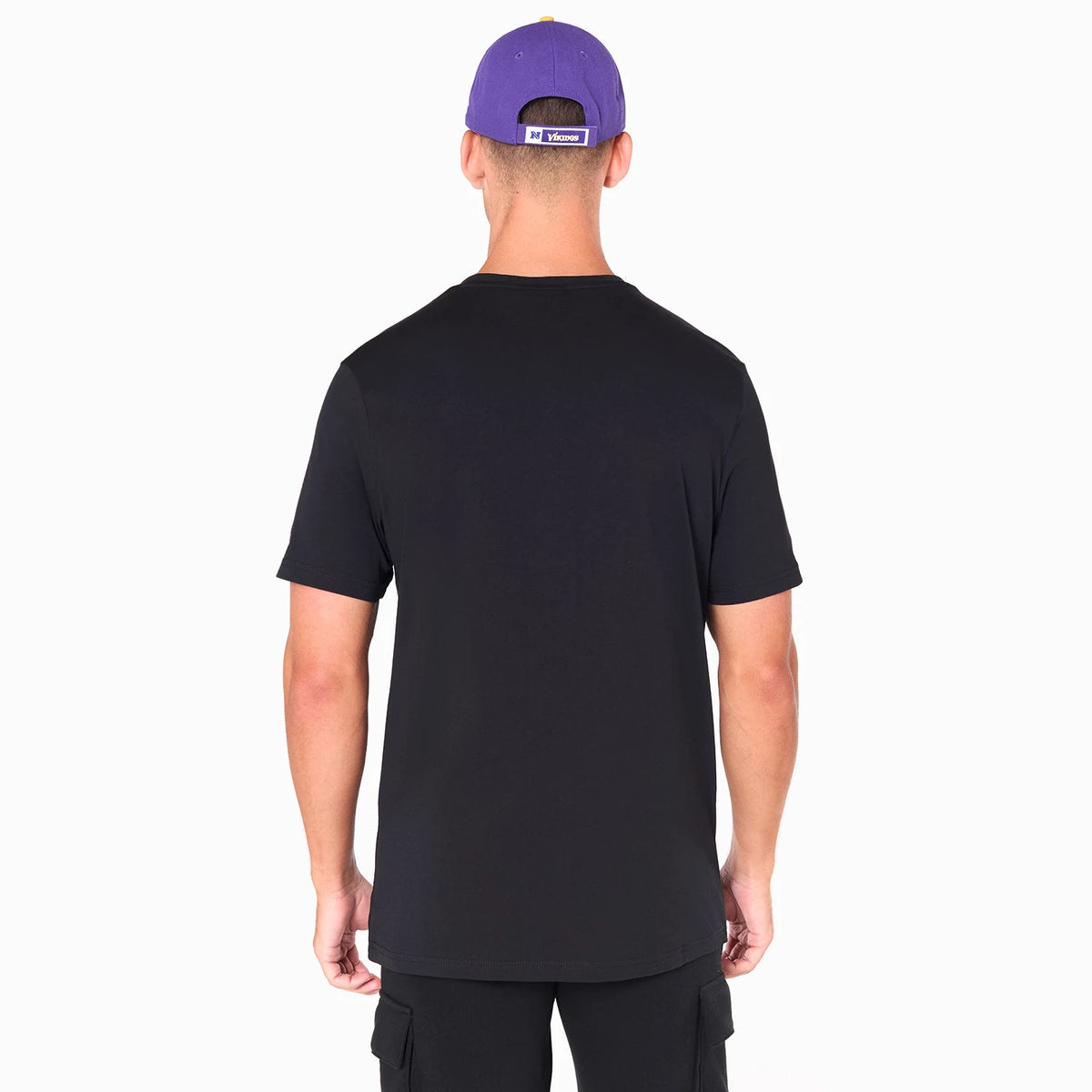 New Era Minnesota Vikings NFL Black T-Shirt, on-model rear view showing the plain black fabric of the back, sleeves, and neckline, paired with a purple cap featuring a raised Vikings logo on the back strap.