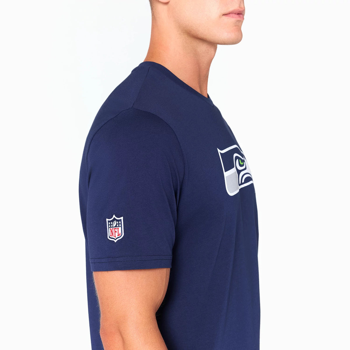 New Era Seattle Seahawks NFL Navy T-Shirt, side view showing the blue fabric with a large printed Seahawks logo on the chest, and an embroidered NFL shield logo on the left sleeve near the shoulder.