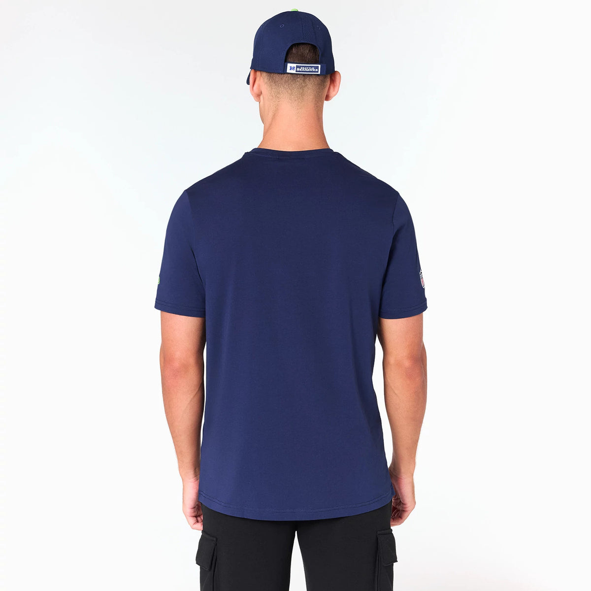 New Era Seattle Seahawks NFL Navy T-Shirt, rear view showing the plain navy back with short sleeves, a small logo on the left sleeve, and a navy cap with an embossed logo worn by a person.