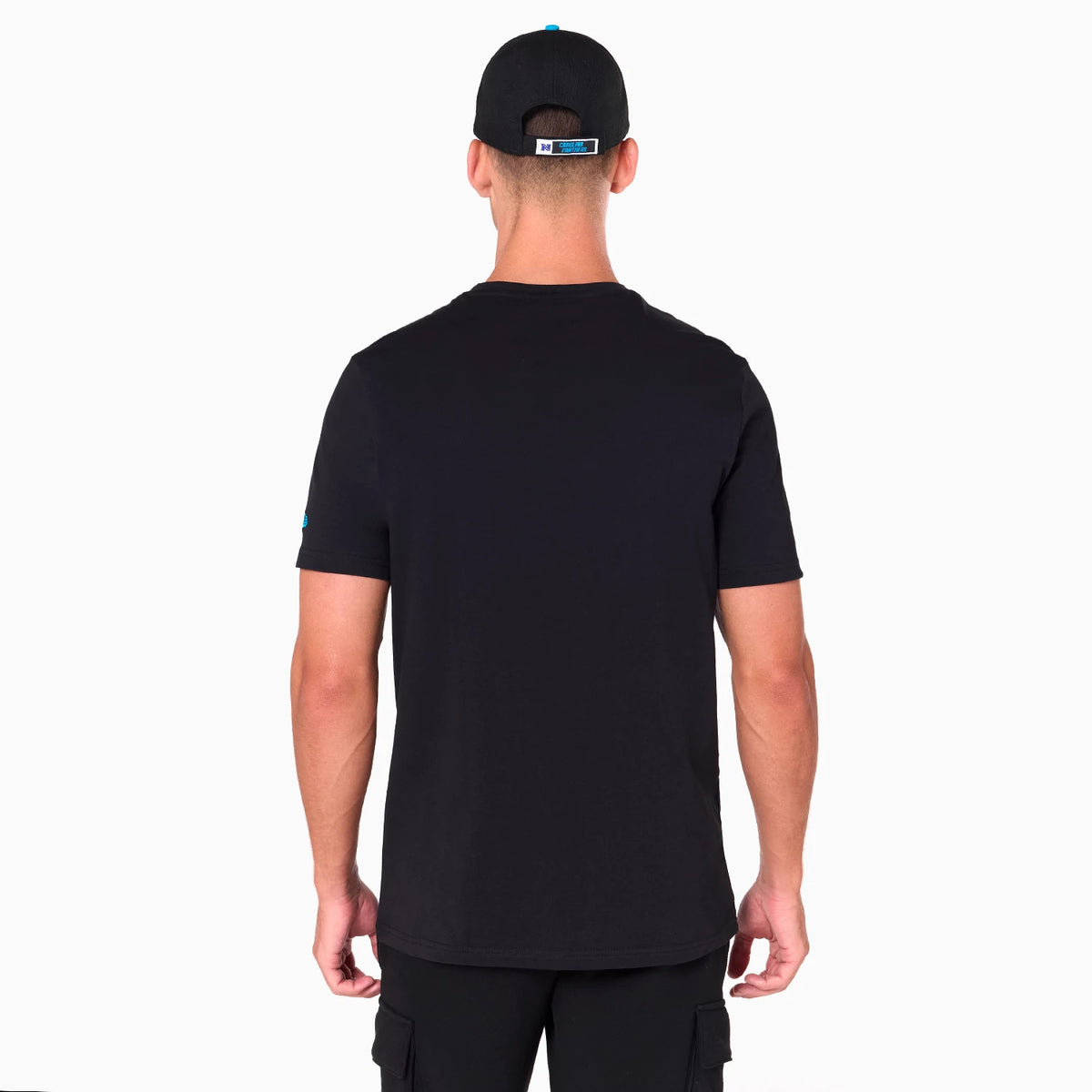 New Era Carolina Panthers NFL Black T-Shirt, rear view showing a plain black back with short sleeves and a small blue logo on the left sleeve, worn by a person also wearing a black cap with a blue embroidered logo above the adjustment strap.