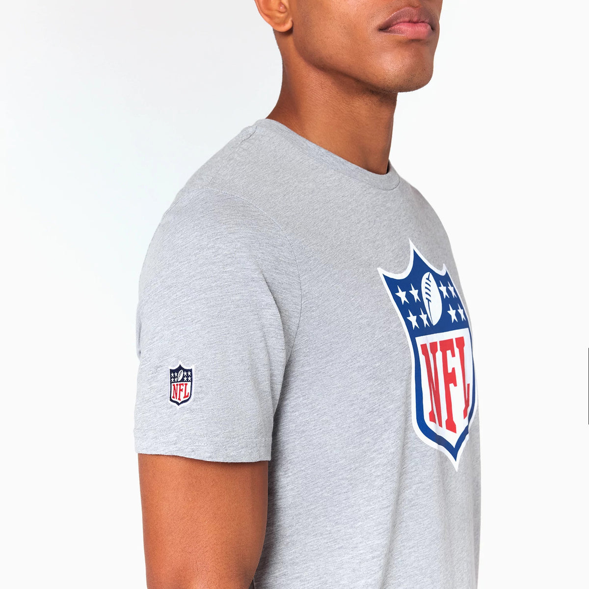 New Era NFL Shield Logo NFL Grey T-Shirt, side view showing the large printed NFL shield logo on the chest in blue, red, and white, with a smaller embroidered NFL logo on the left sleeve of the light grey fabric.