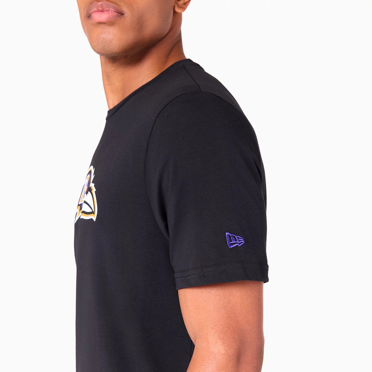 New Era Baltimore Ravens NFL Black T-Shirt, side view showing the short sleeve with a purple embroidered New Era logo near the hem and the large Baltimore Ravens graphic on the chest against the plain black fabric.