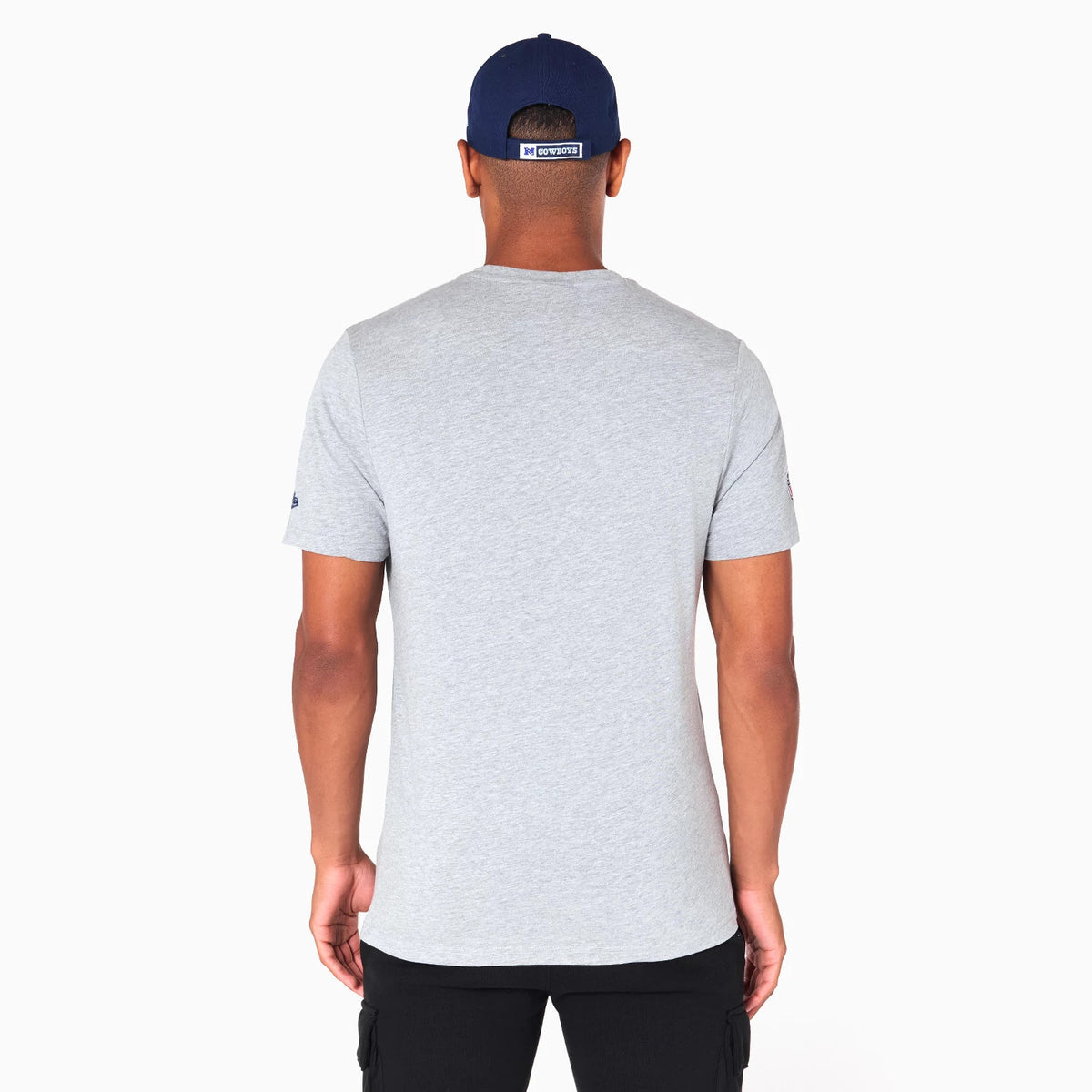 New Era Dallas Cowboys NFL Grey T-Shirt, rear view showing the plain grey fabric extending down to the hem, a small embossed logo on the sleeve, and worn by a person in a dark blue cap with a white embossed logo tag.