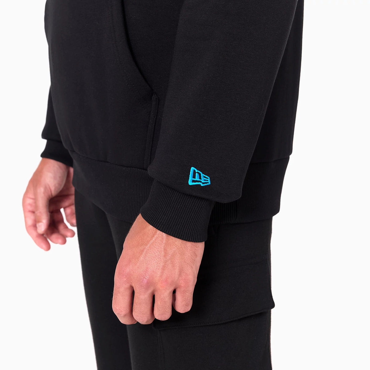 New Era Carolina Panthers NFL Black Pullover Hoodie, three-quarter view showing the cuff with a raised blue New Era logo on the left sleeve and a side pocket detailed on the black hoodie worn by a model.