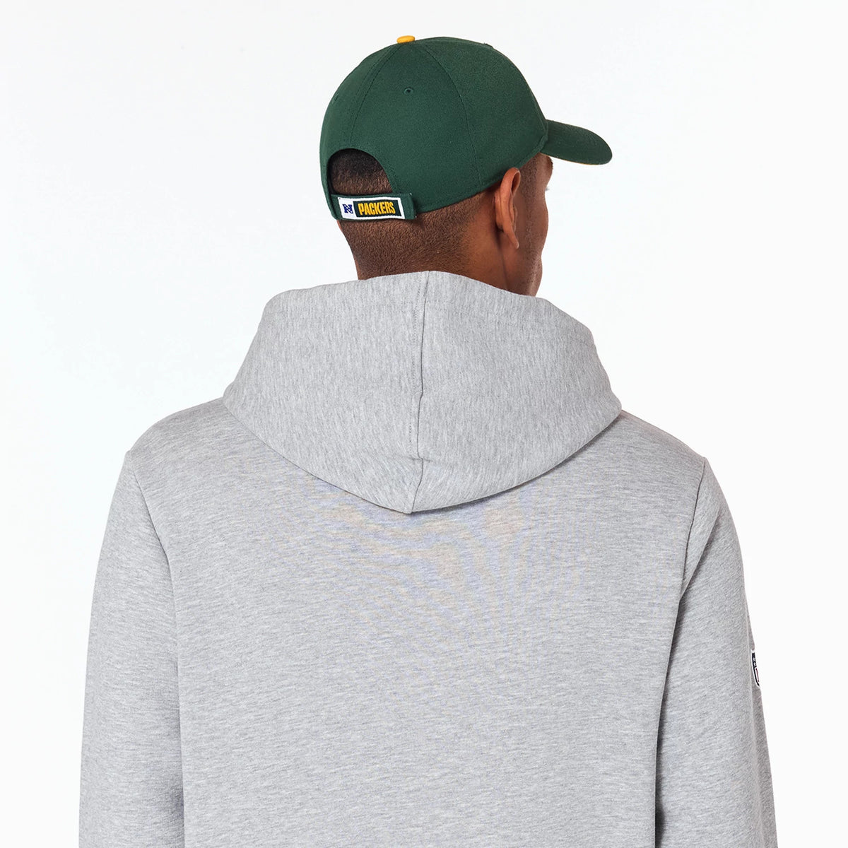 New Era Green Bay Packers NFL Grey Pullover Hoodie, rear view showing the light grey hood and back, with a dark green cap featuring a raised Packers logo patch on the rear strap, worn by a model.