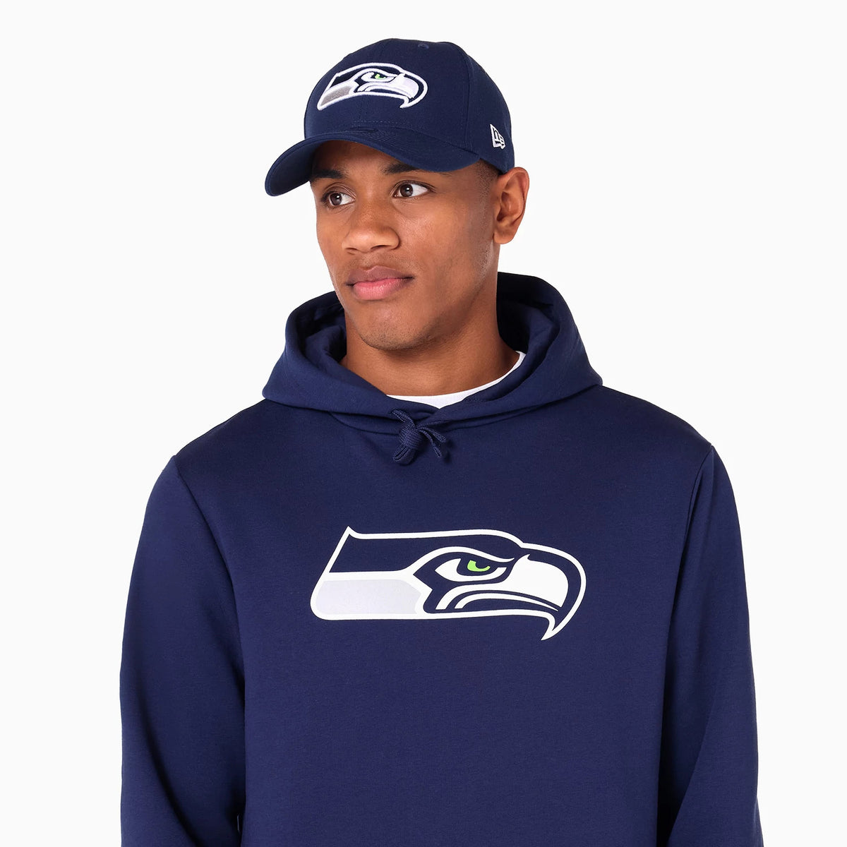 New Era Seattle Seahawks NFL Navy Pullover Hoodie, on-model view showing the navy hoodie with a large white and navy Seahawks logo on the chest, paired with a matching navy cap featuring a raised logo on the front.