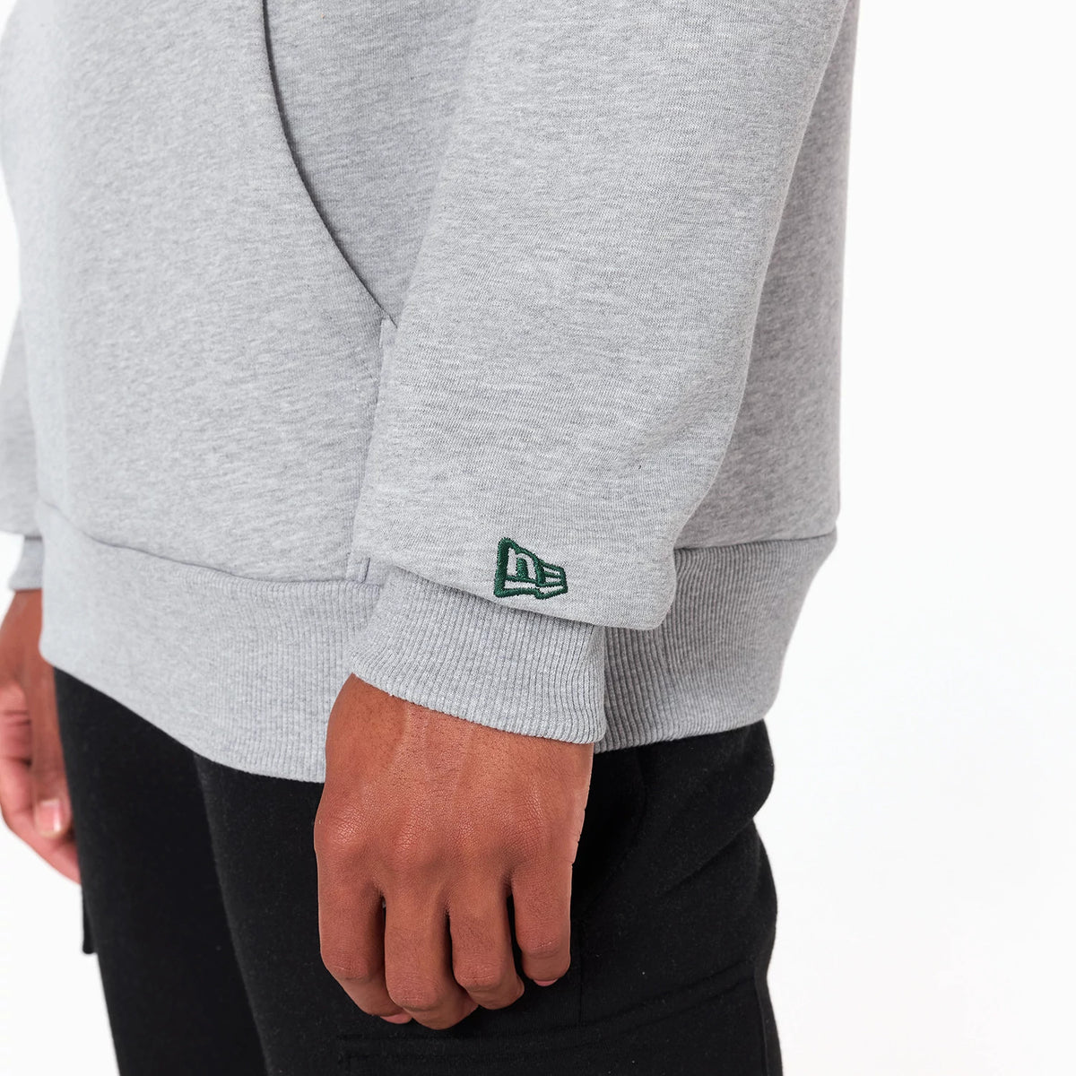 New Era New York Jets NFL Grey Pullover Hoodie, side view showing the grey sleeve with a green embroidered New Era logo near the cuff and a glimpse of the black trousers worn below.