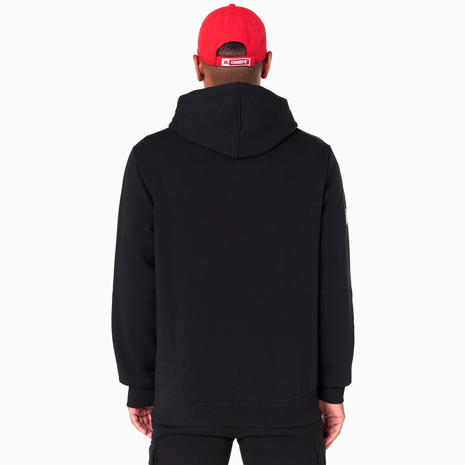 New Era Kansas City Chiefs NFL Black Pullover Hoodie, rear view showing the plain black back with a relaxed hood, worn by a model also wearing a red cap with a raised Chiefs logo on the back.