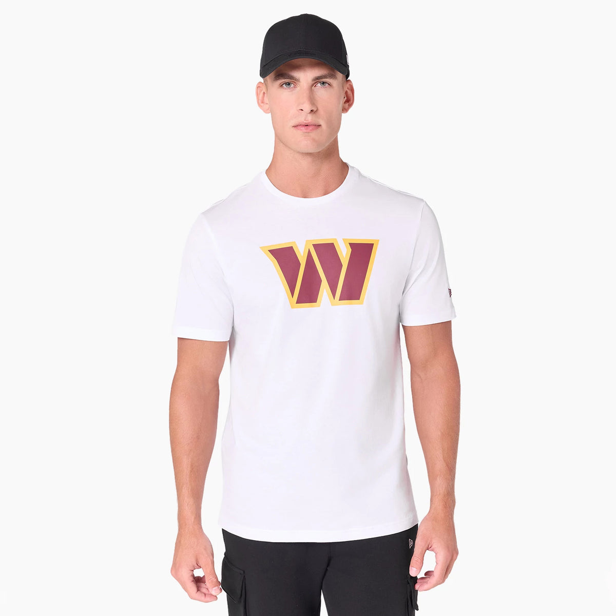 New Era Washington Commanders NFL White T-Shirt, on-model view displaying a large maroon and yellow W logo printed on the chest with short sleeves and a relaxed fit, paired with black trousers and a black cap.