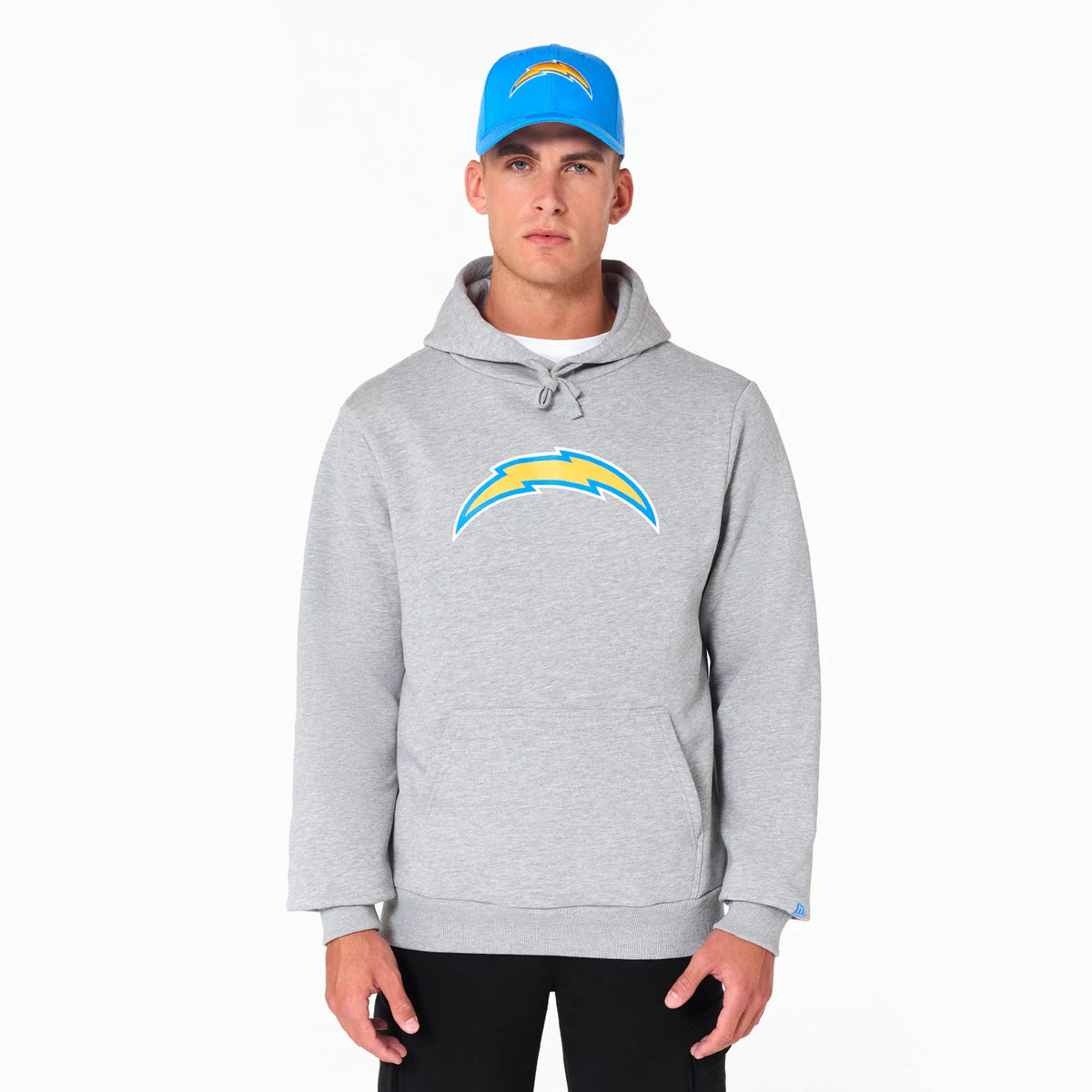 New Era LA Chargers NFL Grey Pullover Hoodie, on-model view highlighting the large blue and yellow LA Chargers logo centred on the chest, a spacious front pocket, and the hood with drawstrings, worn with a blue cap featuring the same logo.