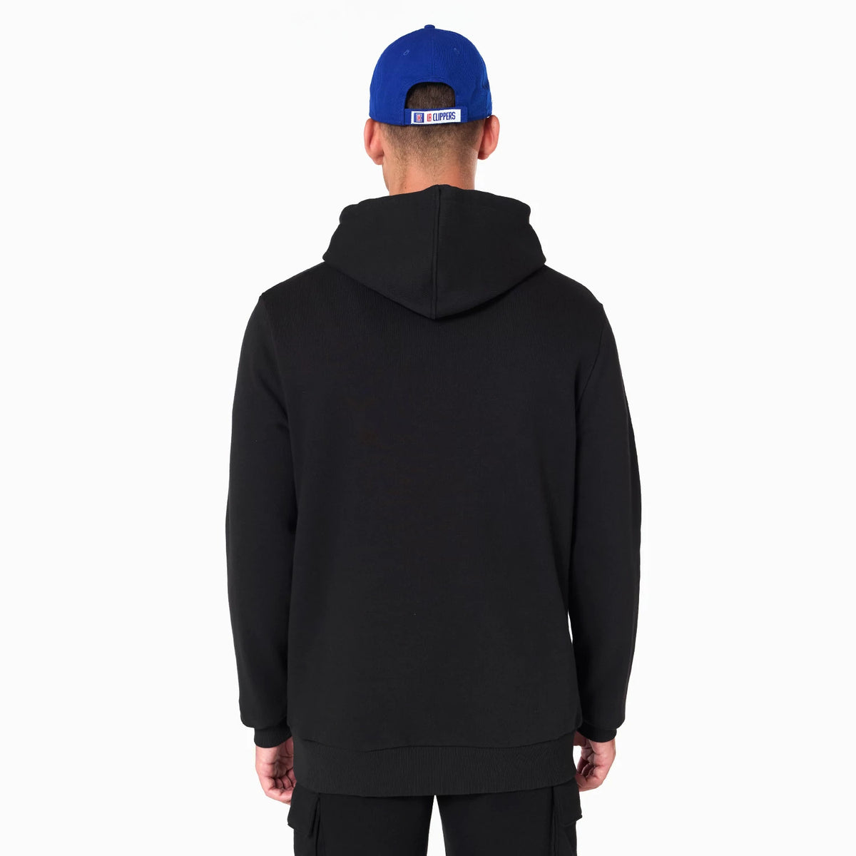 New Era LA Clippers NBA Black Pullover Hoodie, on-model rear view showcasing the plain black back with a relaxed hood, worn with a blue cap featuring a debossed LA Clippers logo on the strap at the back.
