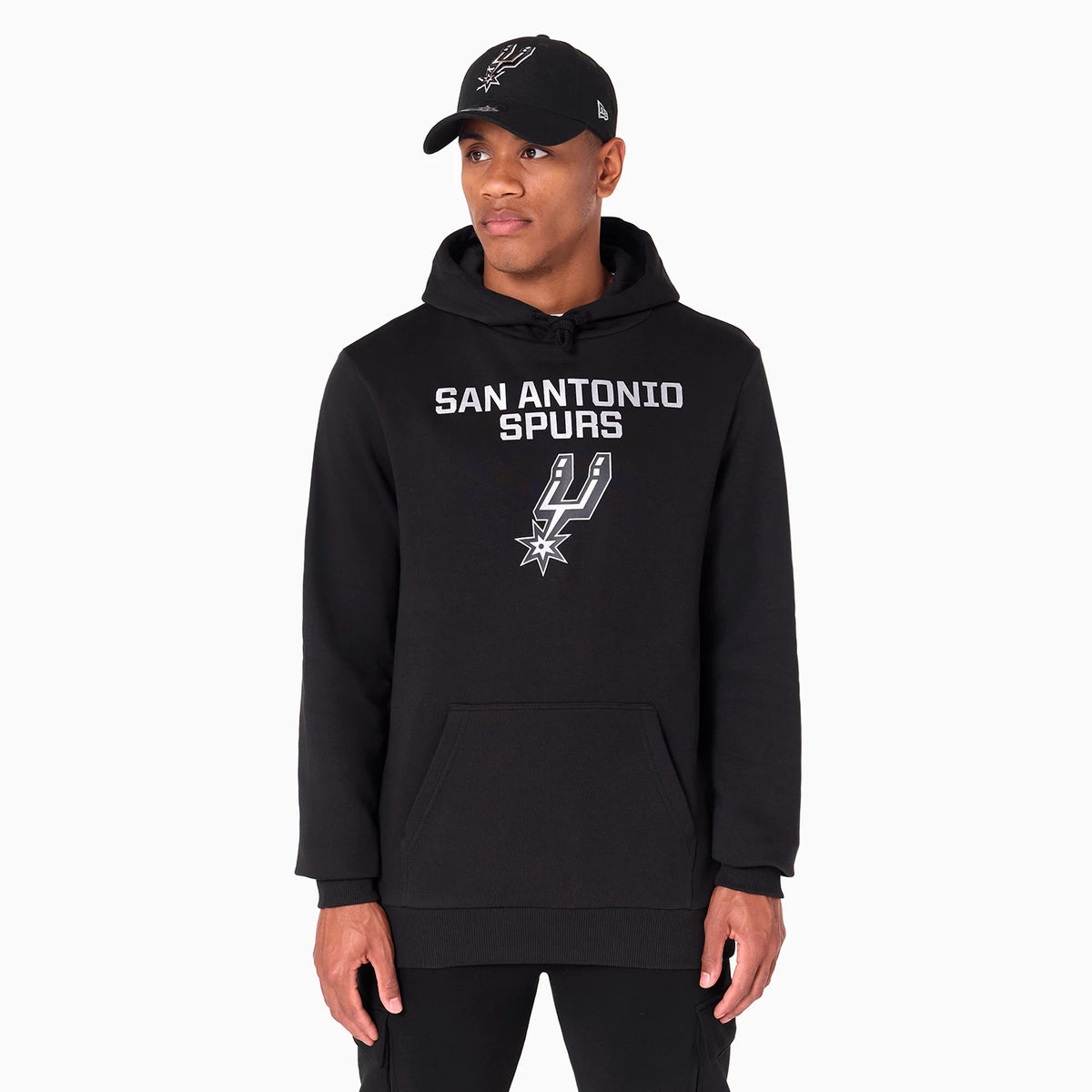 New Era San Antonio Spurs NBA Black Pullover Hoodie, on-model view showing the black hoodie with the San Antonio Spurs logo and text centred on the chest, and a raised New Era logo on a black cap worn by the model.