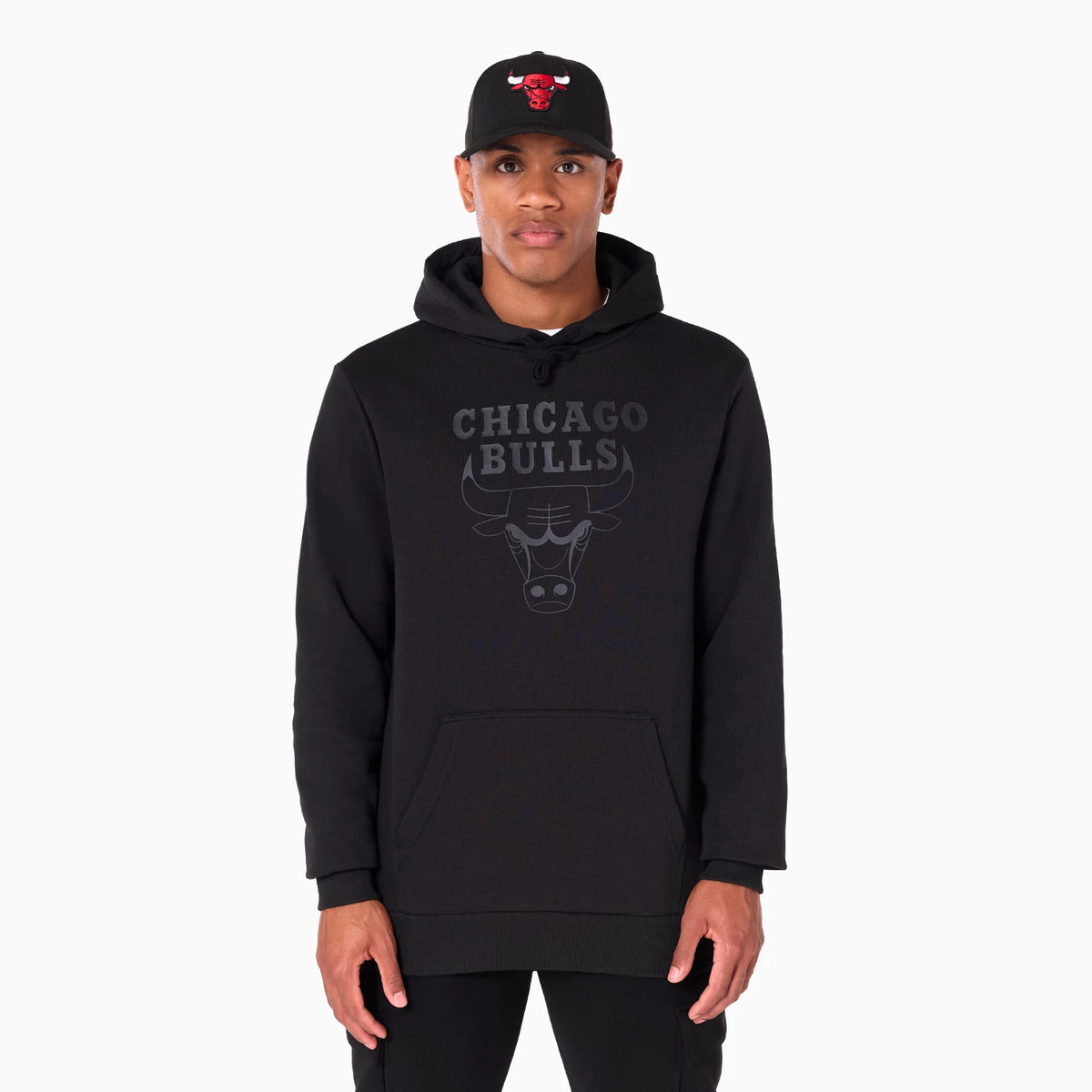 New Era Chicago Bulls NBA Black Pullover Hoodie, on-model view showing the black hoodie with a large front pocket, featuring a grey Chicago Bulls graphic centred on the chest, worn by a person also wearing a black cap with a red raised Bulls logo.