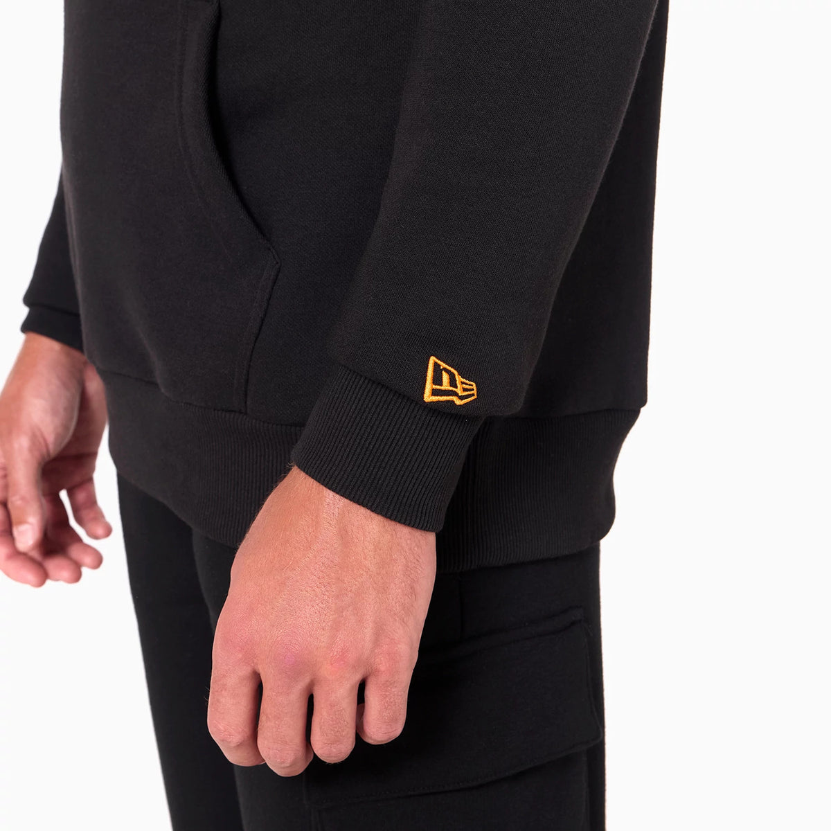 New Era Phoenix Suns NBA Black Pullover Hoodie, side view showing the lower half with a small pocket, ribbed cuffs, and an orange embroidered New Era logo on the cuff of the sleeve.