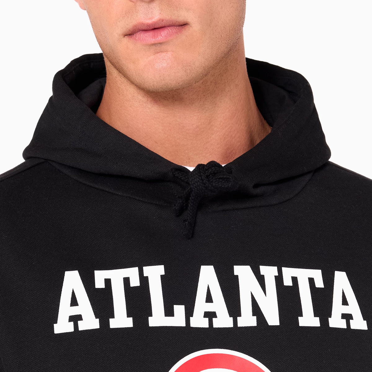 New Era Atlanta Hawks NBA Black Pullover Hoodie, front view showing the black hoodie hood with drawstrings and large white ATLANTA lettering across the chest, partially obscured by the model's arm.