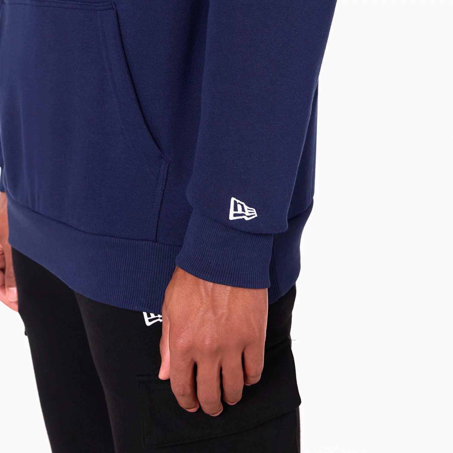 New Era New Orleans Pelicans NBA Navy Pullover Hoodie, on-model view showing the close-up of the navy fabric, ribbed cuff with a white embroidered New Era logo near the edge and a side pocket detail on the body of the garment.