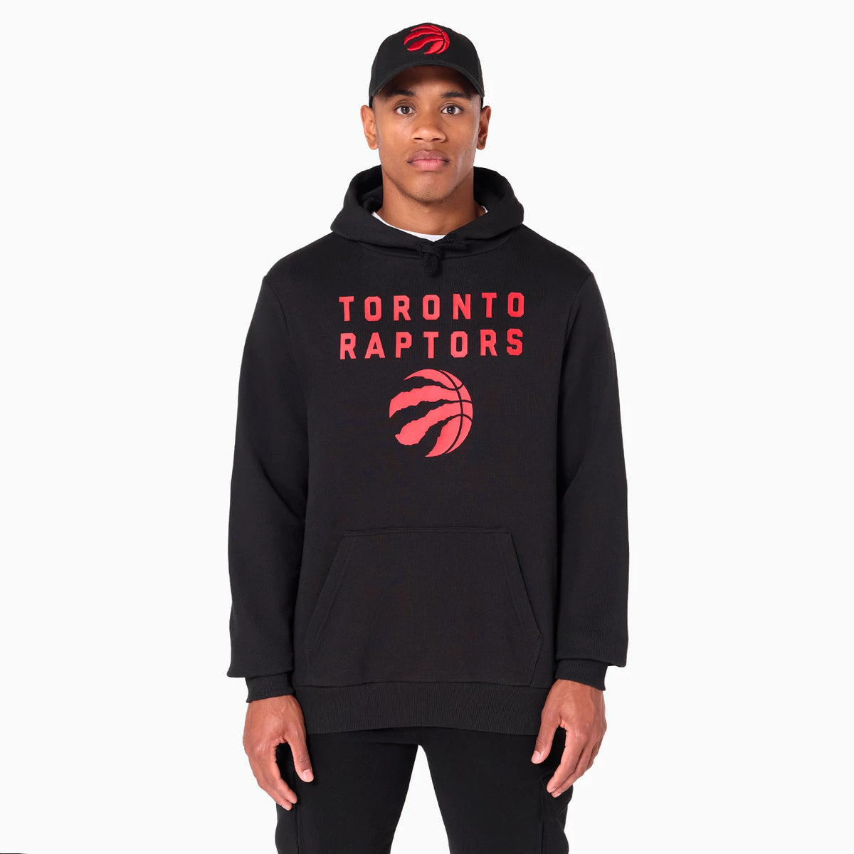New Era Toronto Raptors NBA Black Pullover Hoodie, front view showing large red Toronto Raptors text and logo centred on the chest, with a black cap featuring a raised red Raptors logo worn by the model.