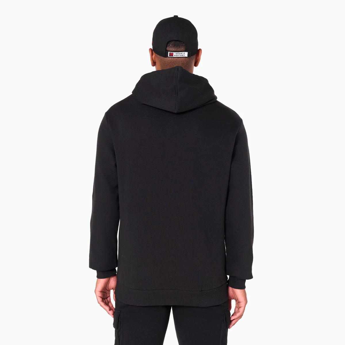 New Era Toronto Raptors NBA Black Pullover Hoodie, rear view showing the relaxed fit black hoodie with a spacious hood, worn by a model along with a black cap featuring an embroidered patch on the back.