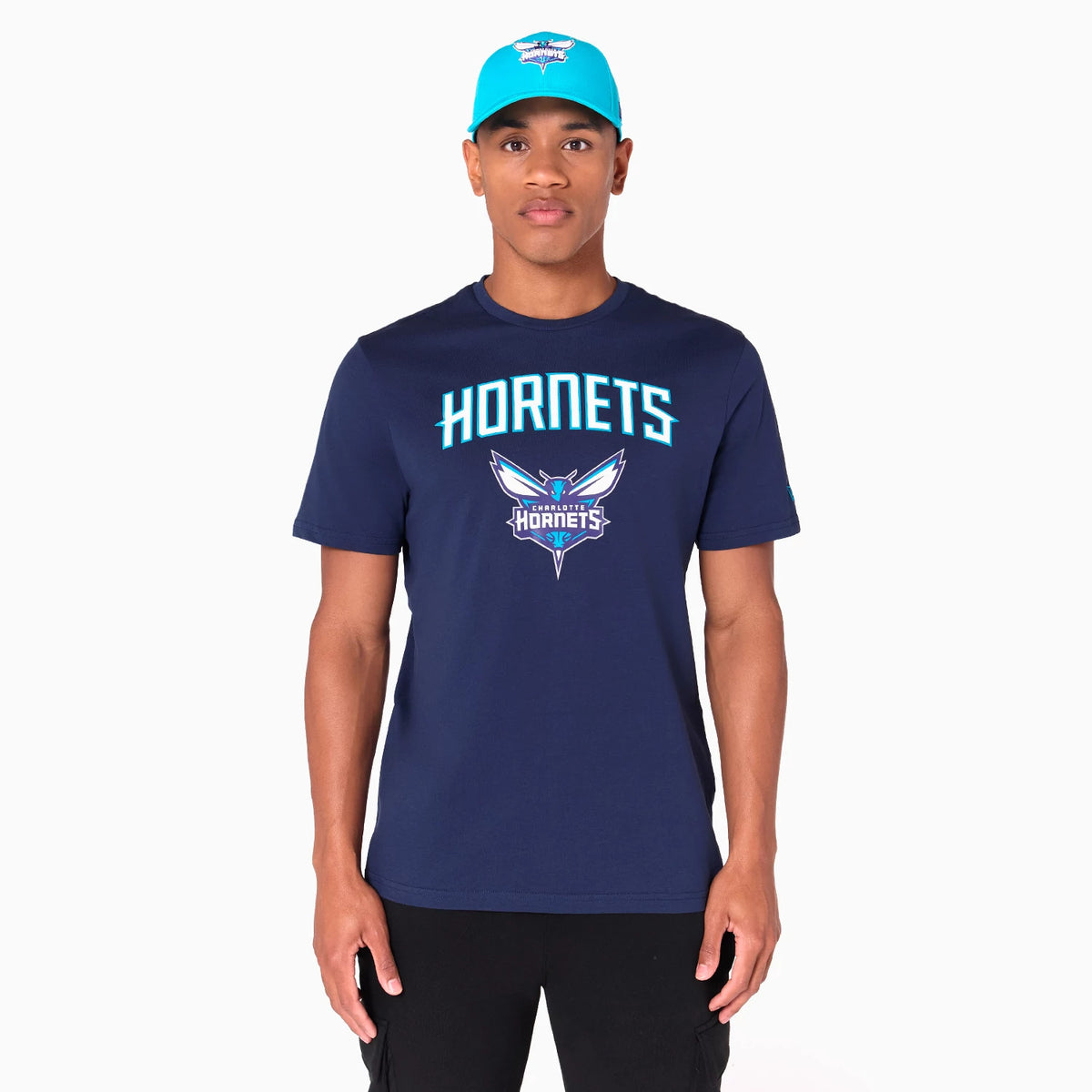 New Era Charlotte Hornets NBA Navy T-Shirt, on-model view showing the navy shirt with HORNETS printed across the chest in blue and a detailed Hornets logo beneath, paired with a turquoise cap featuring a raised Charlotte Hornets logo.