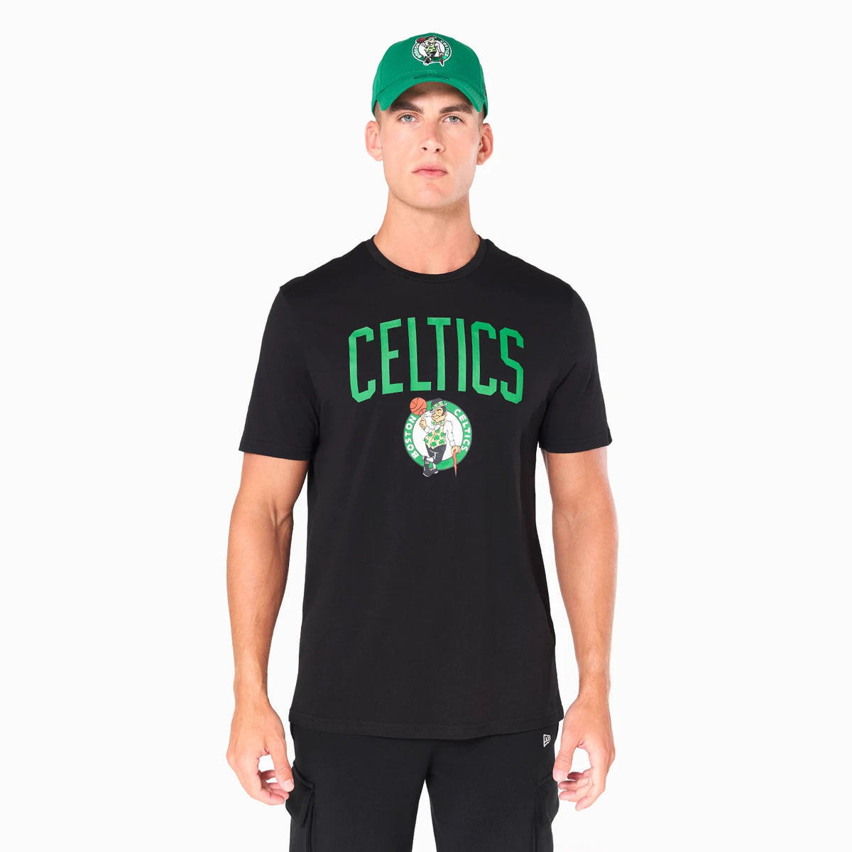 New Era Boston Celtics NBA Black T-Shirt, front view showing the black T-shirt with large green CELTICS text across the chest above the team logo, worn by a model with a green cap featuring a debossed logo.