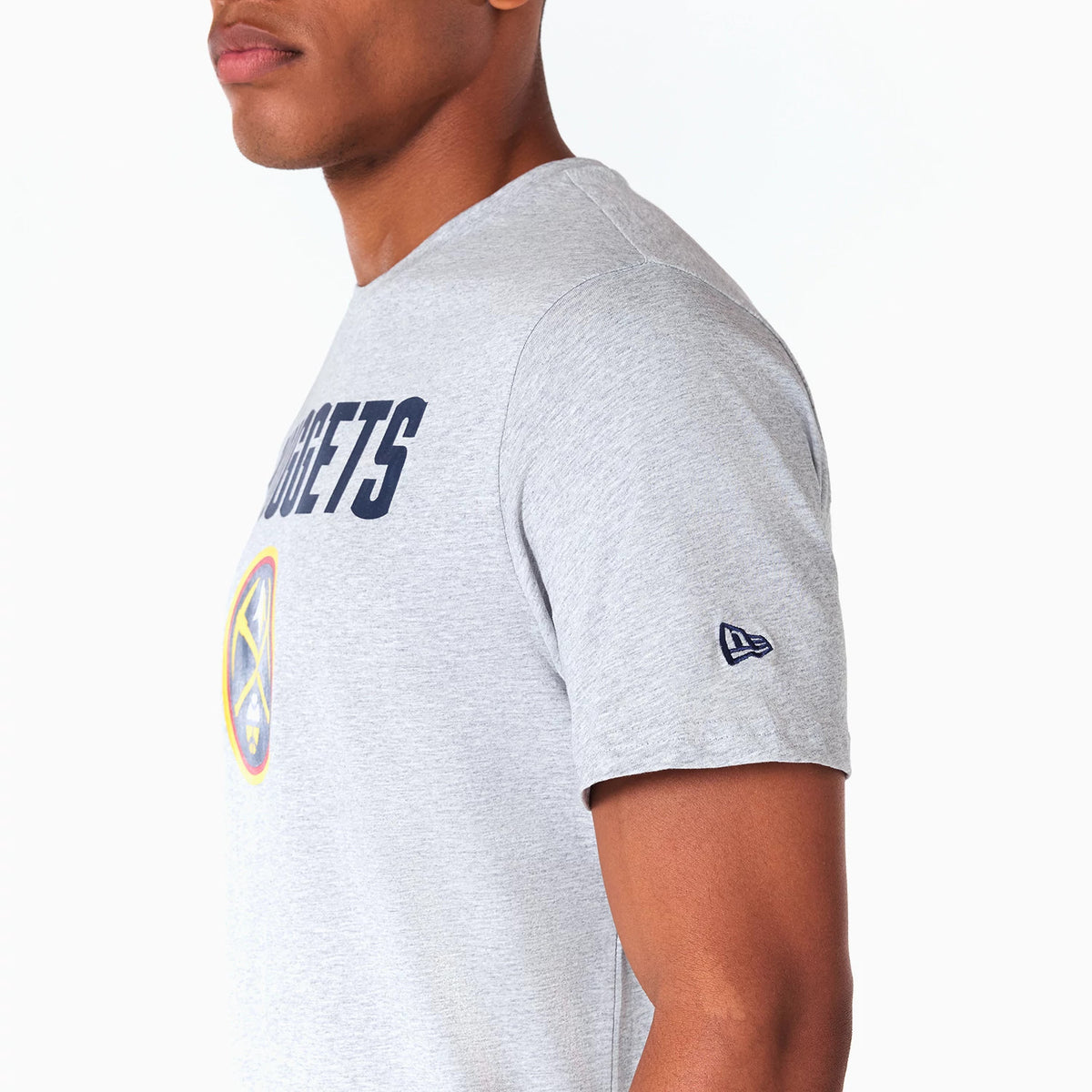New Era Denver Nuggets NBA Grey T-Shirt, side view showing the light grey fabric with navy NUGGETS text on the chest, a colourful Denver Nuggets logo below it, and a raised New Era logo on the left sleeve near the shoulder.