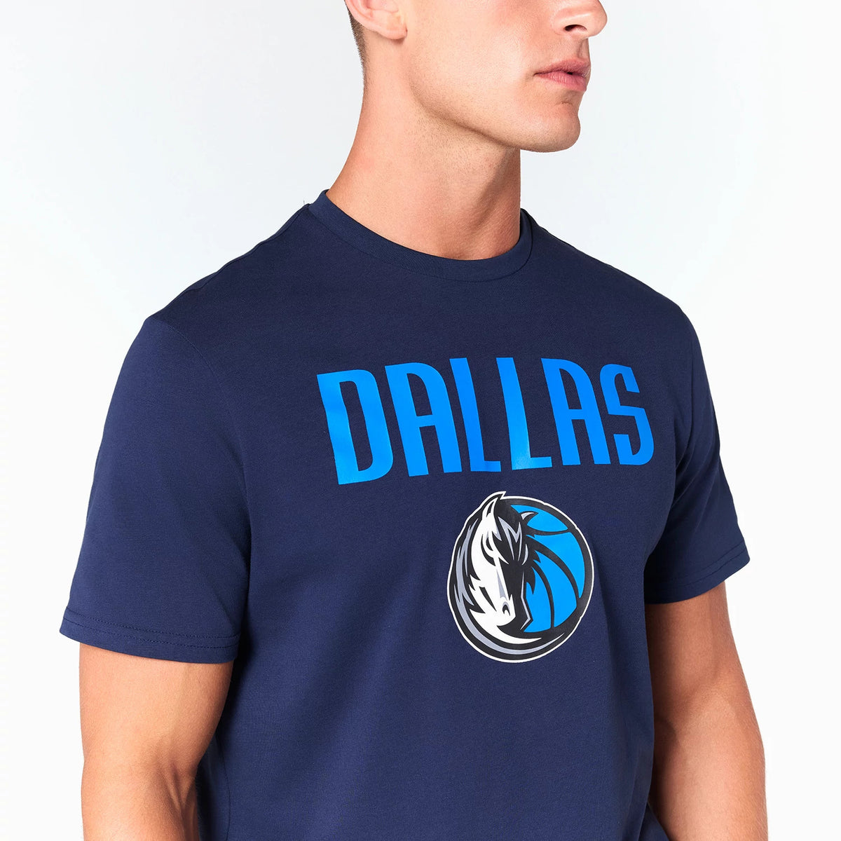 New Era Dallas Mavericks NBA Navy T-Shirt, on-model view showing the bold blue DALLAS lettering across the chest above the team logo featuring a horse head in black and white with blue accents centred beneath the text.