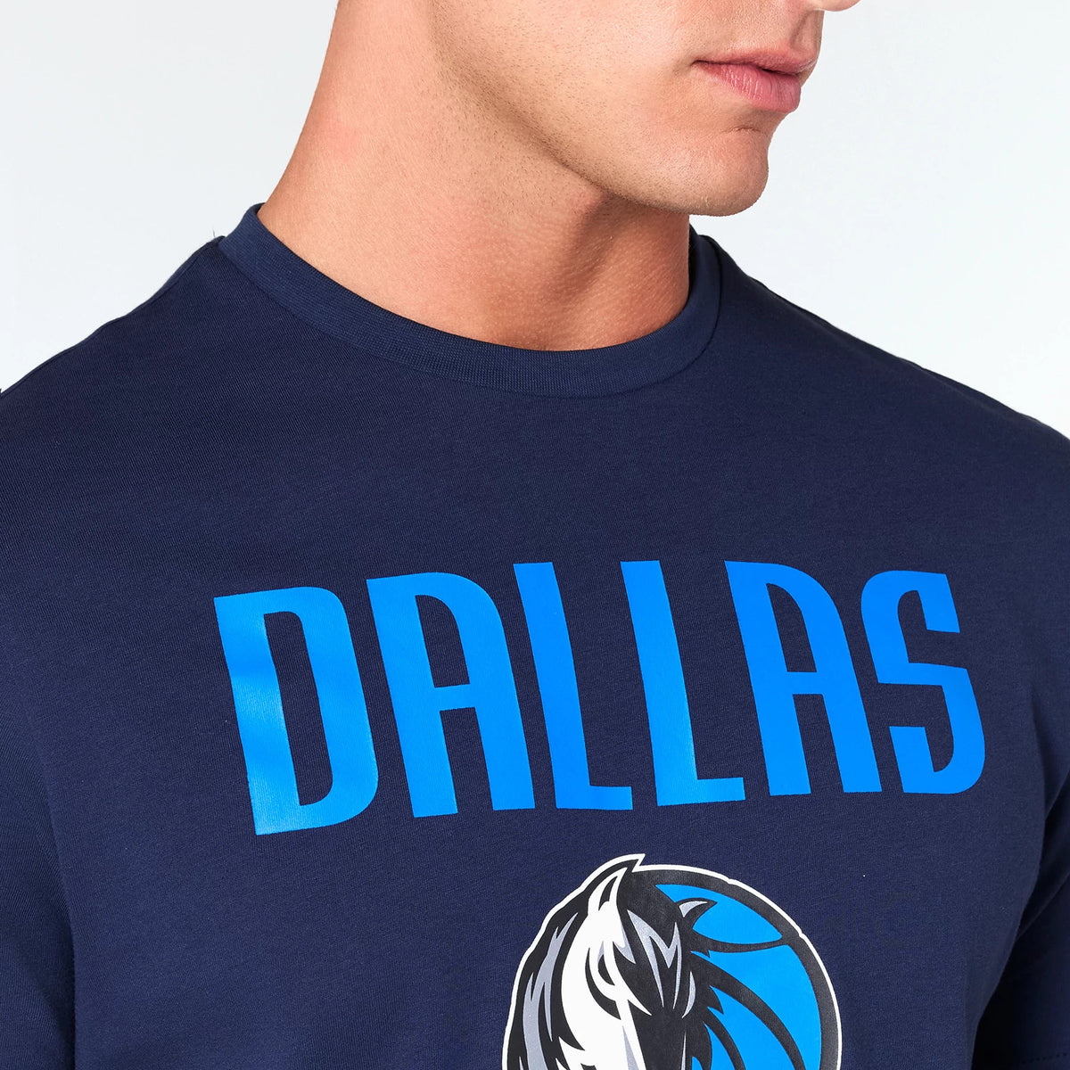 New Era Dallas Mavericks NBA Navy T-Shirt, on-model showing the upper part of a navy shirt with a large front print featuring DALLAS in bold blue letters and the Mavericks' logo below it on the chest.