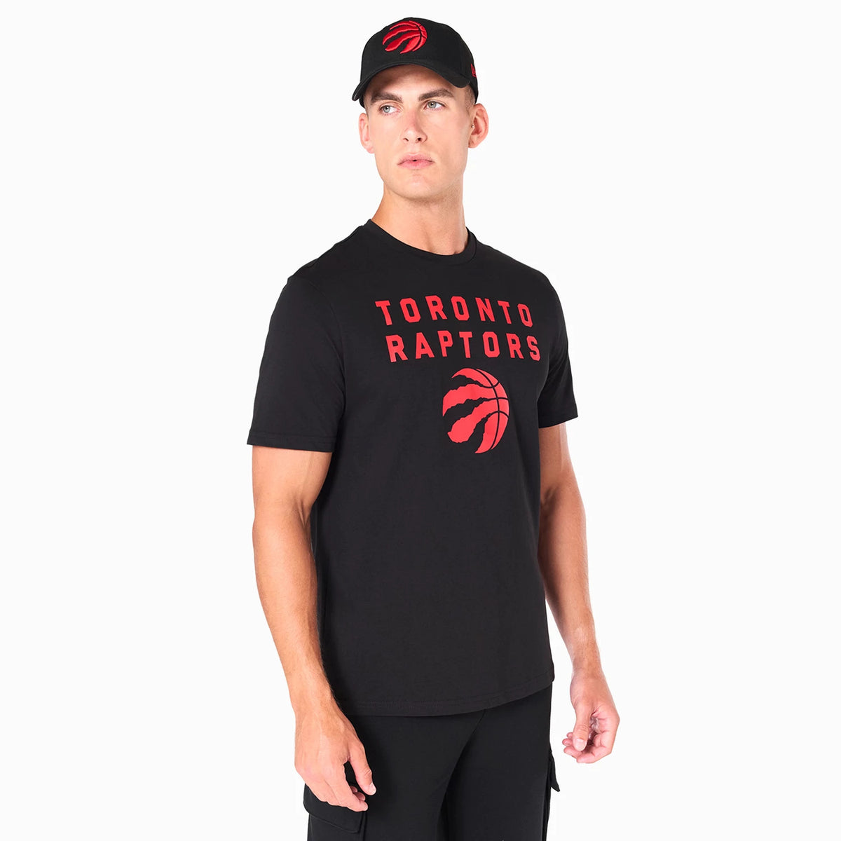 New Era Toronto Raptors NBA Black T-Shirt, on-model view showing the black tee with TORONTO RAPTORS in red across the chest and a red raptor claw logo beneath, paired with a black cap featuring a raised red raptor claw on the front.