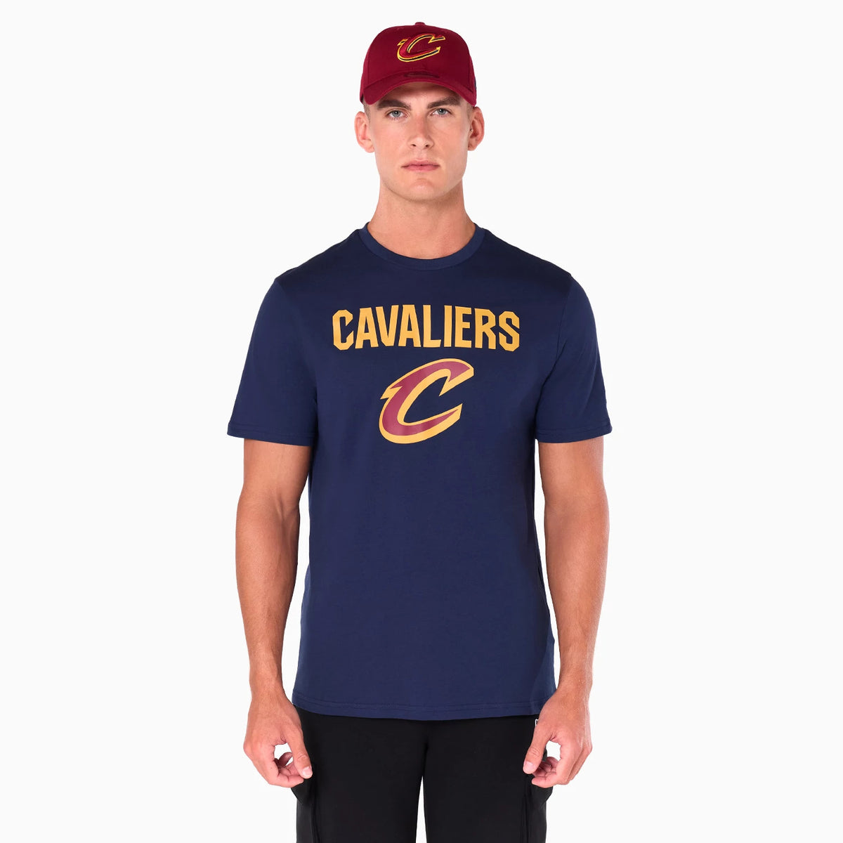 New Era Cleveland Cavaliers NBA Navy T-Shirt, on-model view featuring a navy t-shirt with Cavaliers in gold lettering and a large Cavaliers logo below, paired with a red cap displaying a raised logo on the front.