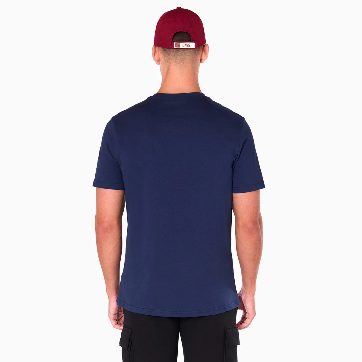 New Era Cleveland Cavaliers NBA Navy T-Shirt, rear view showing the plain navy fabric with short sleeves, a man wearing a red cap that has a raised New Era logo and CAVS text on the back above the adjustable strap.