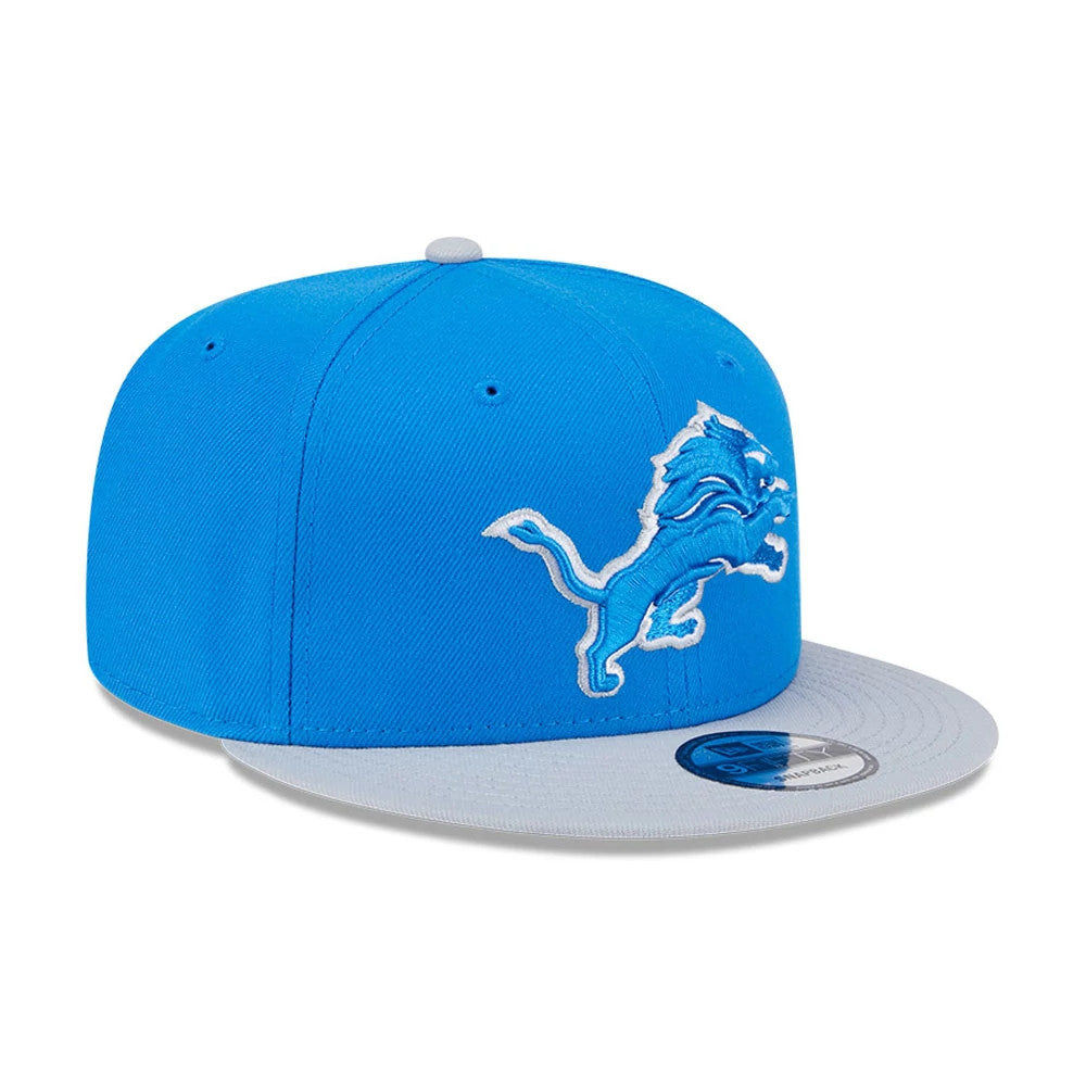 Detroit Lions NFL Evergreen Blue New Era 9FIFTY Snapback Adjustable Cap, three-quarter view showing the raised embroidered lion logo on the front blue panel, with a contrasting grey visor and a 9FIFTY size sticker on top.