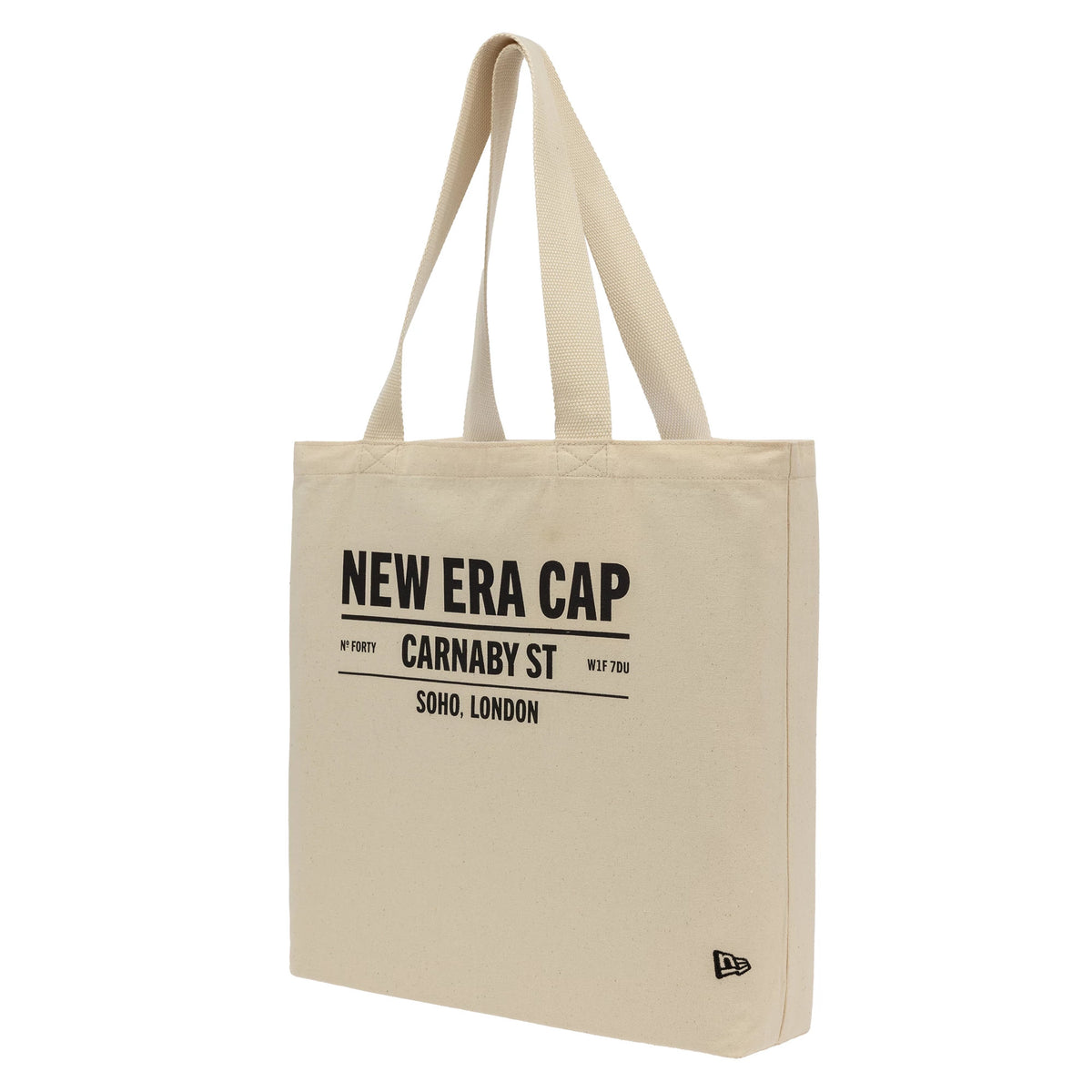 New Era Cap Carnaby Address Light Beige Canvas Tote Bag, three-quarter view showing the light beige tote with black printed text centred on the side, long handles extending from the top, and a small raised New Era logo in the bottom corner.