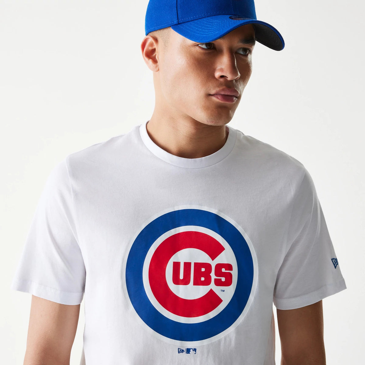 New Era Chicago Cubs MLB Regular White T-Shirt, on-model view showing the large Cubs logo centred on the chest in red and blue, a blue embroidered New Era logo on the left sleeve, and worn with a solid blue cap.