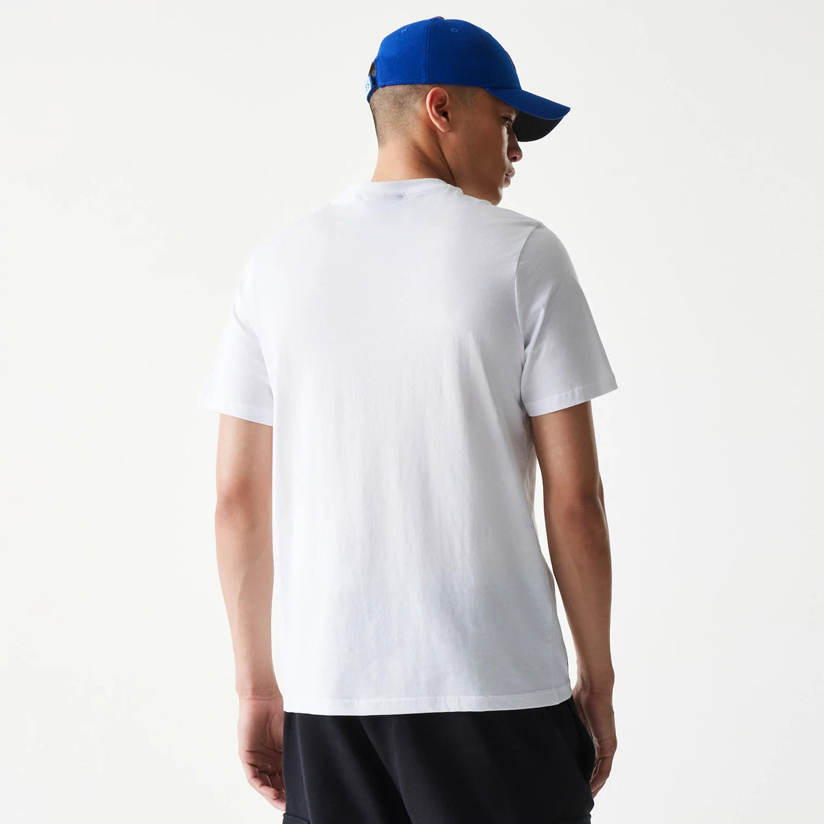 New Era Chicago Cubs MLB Regular White T-Shirt, rear view showing a plain white back with short sleeves, worn by a person in black trousers and a blue cap featuring a raised logo on the back.