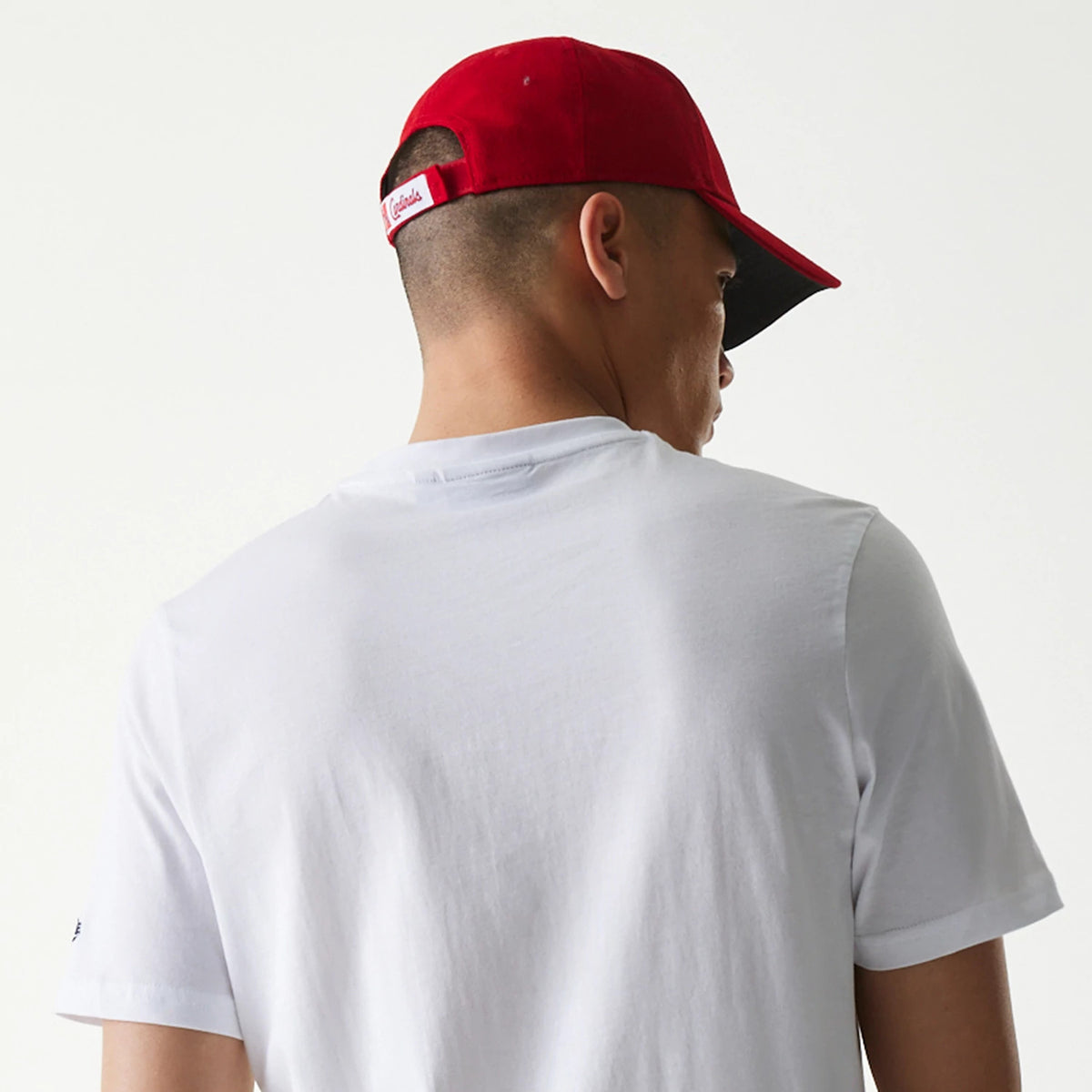 New Era St. Louis Cardinals MLB Regular White T-Shirt, on-model view showing the plain white back of the T-shirt, a red cap worn by the model featuring a debossed Cardinals logo on the rear adjustment strap.