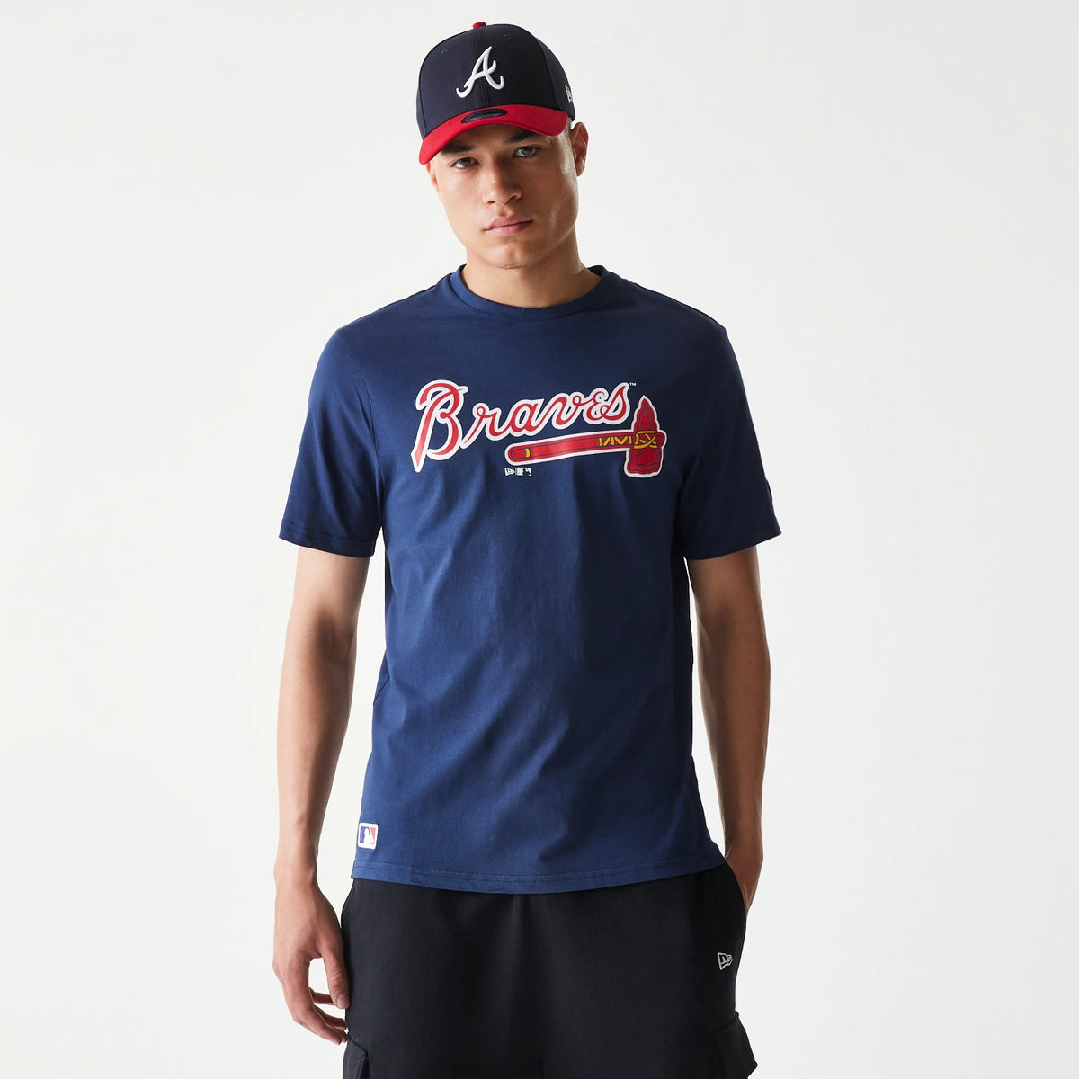 New Era Atlanta Braves MLB Regular Dark Blue T-Shirt, on-model view showing the dark blue tee with the large red and white Braves logo centred on the chest, paired with a black and red cap featuring a raised white New Era logo on the front.