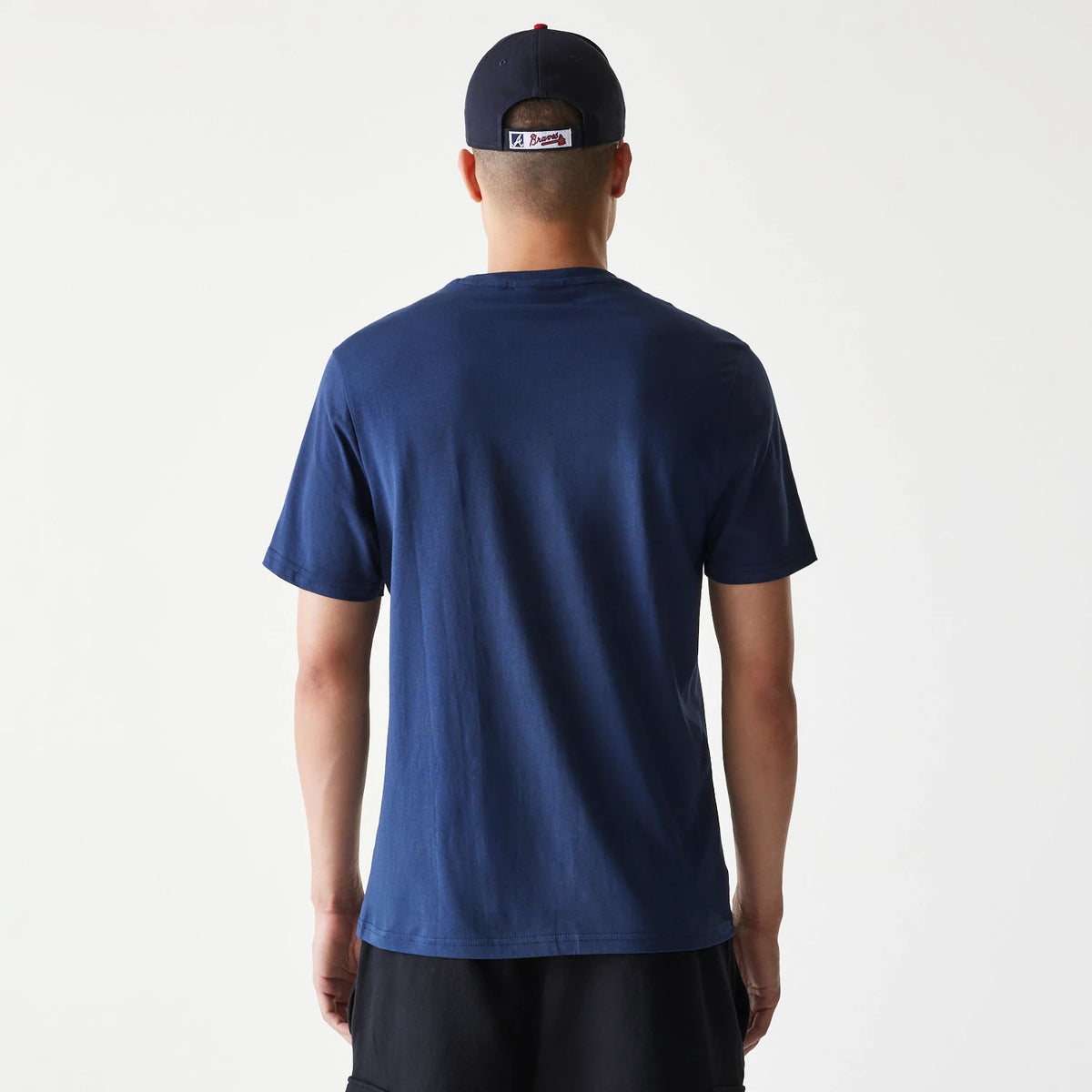 New Era Atlanta Braves MLB Regular Dark Blue T-Shirt, rear view showing the plain dark blue back with short sleeves, worn by a model with a dark blue cap featuring a raised MLB Braves logo centred above the rear opening.