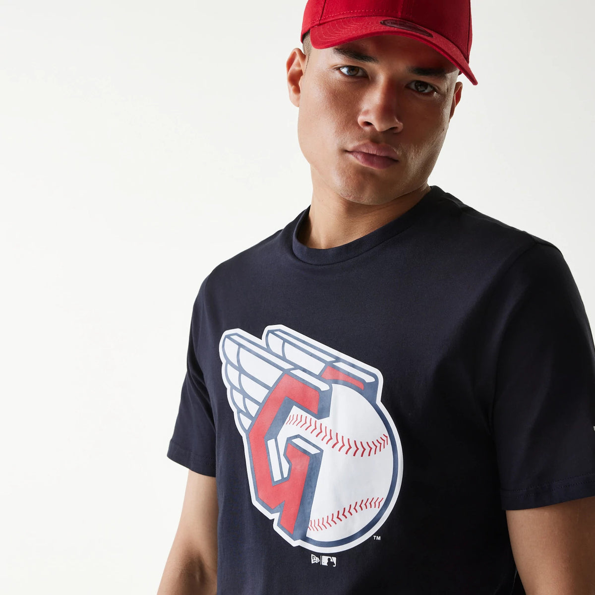 New Era Cleveland Guardians MLB Regular Navy T-Shirt, on-model view showing the navy shirt with a large Cleveland Guardians logo printed in red and white on the chest, worn by a person in a red cap.