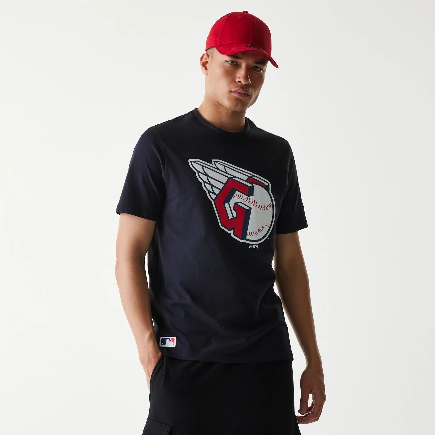 New Era Cleveland Guardians MLB Regular Navy T-Shirt, on-model view showing a large team logo printed on the chest in red, white, and grey, worn with a contrasting red cap, highlighting the navy colour of the shirt.