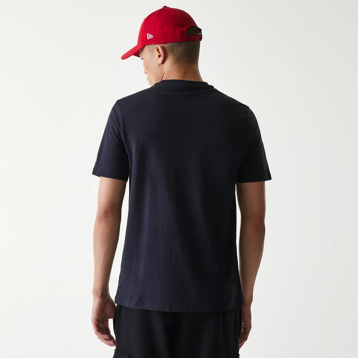 New Era Cleveland Guardians MLB Regular Navy T-Shirt, on-model view showing the plain navy back of the shirt, paired with a bright red cap featuring a debossed New Era logo on the side, cap worn by model.