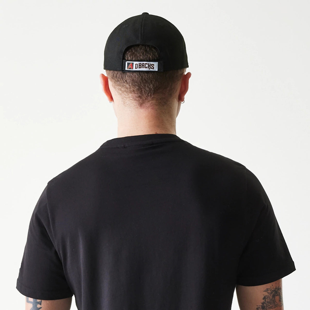 New Era Arizona Diamondbacks MLB Regular Black T-Shirt, rear view showing a black T-shirt worn under a black cap with a raised logo label centred above the back opening, the image captures the simple design of the shirt and cap.