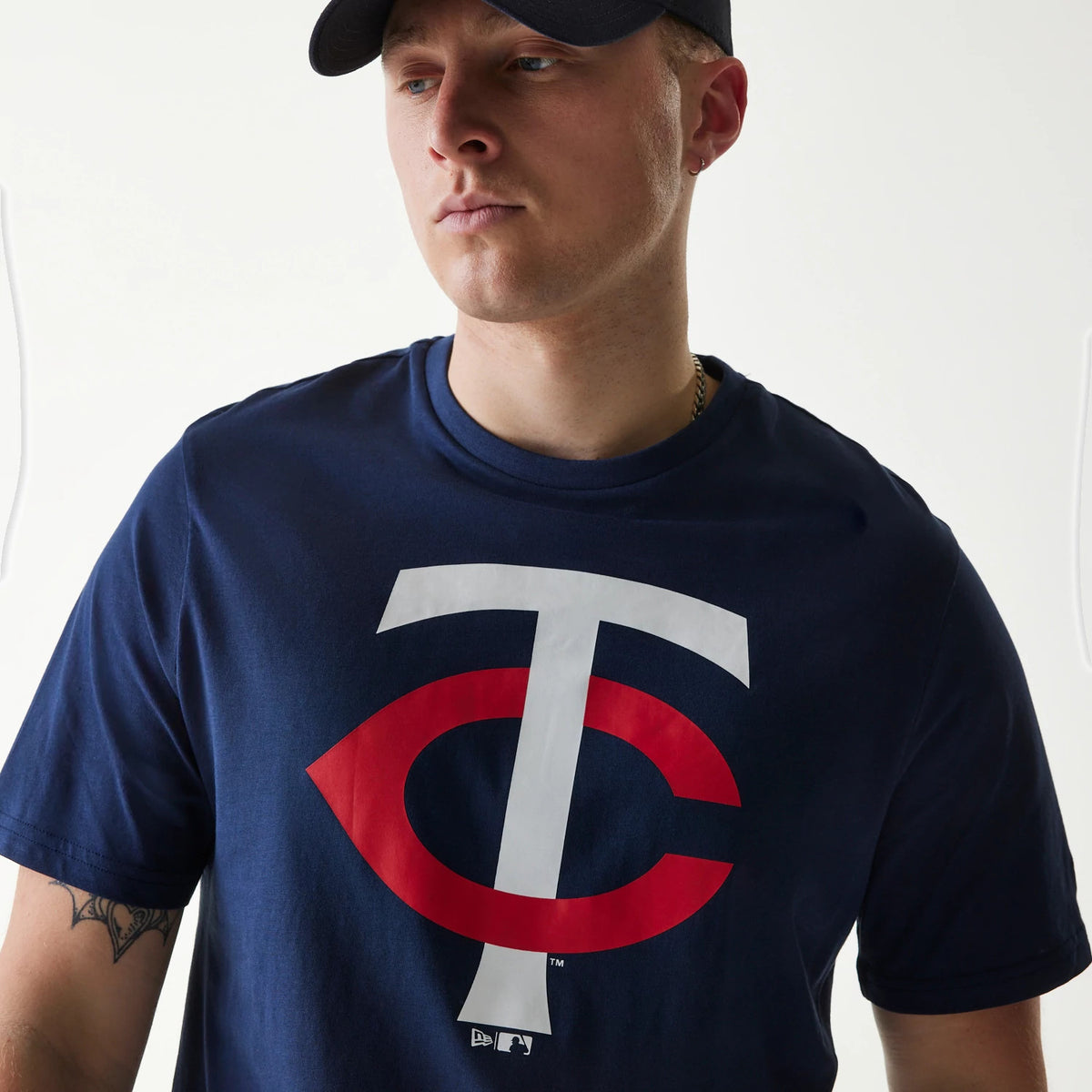 New Era Minnesota Twins MLB Regular Dark Blue T-Shirt, on-model view showing a large white and red logo centred on the chest, worn by a person in a black cap with a debossed New Era logo on the front of the cap.