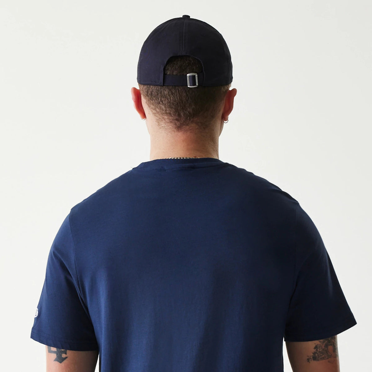 New Era Minnesota Twins MLB Regular Dark Blue T-Shirt, rear view showing the plain dark blue back with short sleeves, a man wearing the shirt along with a dark cap strapped at the back, both fitting closely to the body.