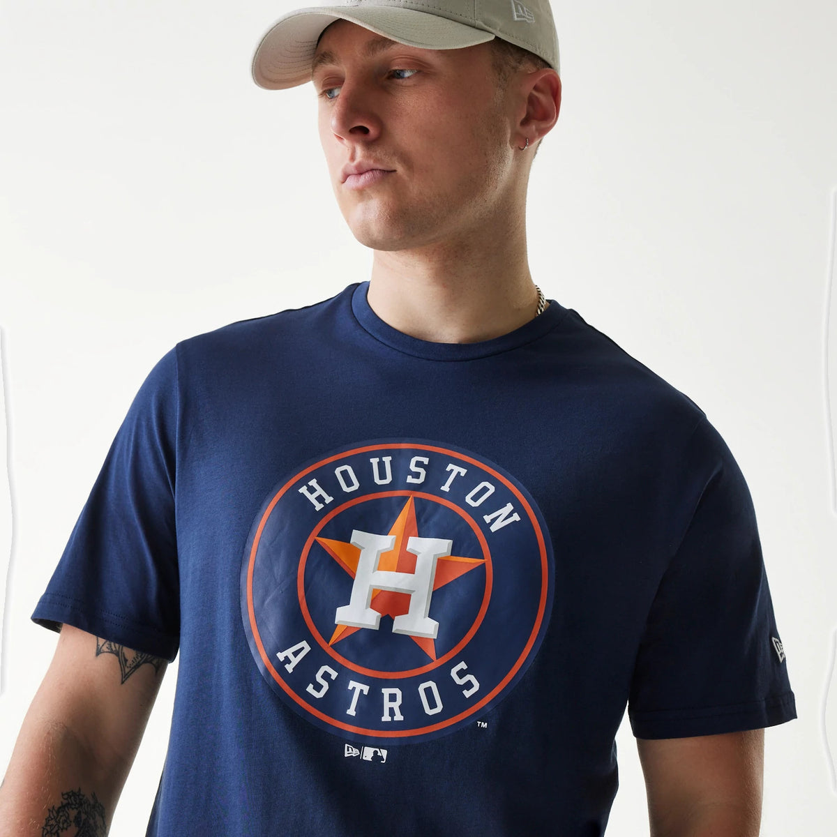 New Era Houston Astros MLB Regular Dark Blue T-Shirt, front view showing a large Houston Astros logo printed in orange and white on the chest, worn by a person with a light beige cap featuring a raised New Era logo on the side.