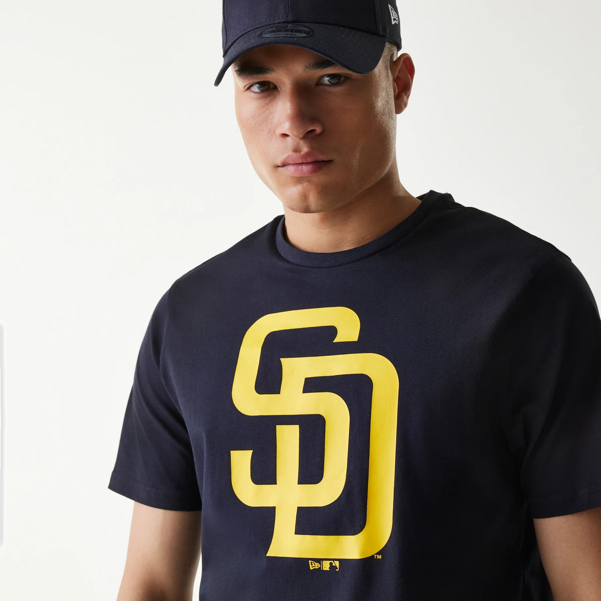 New Era San Diego Padres MLB Regular Navy T-Shirt, front view showing the large yellow SD logo printed on the chest, a man wearing the navy shirt paired with a navy cap featuring a debossed New Era logo on the side.
